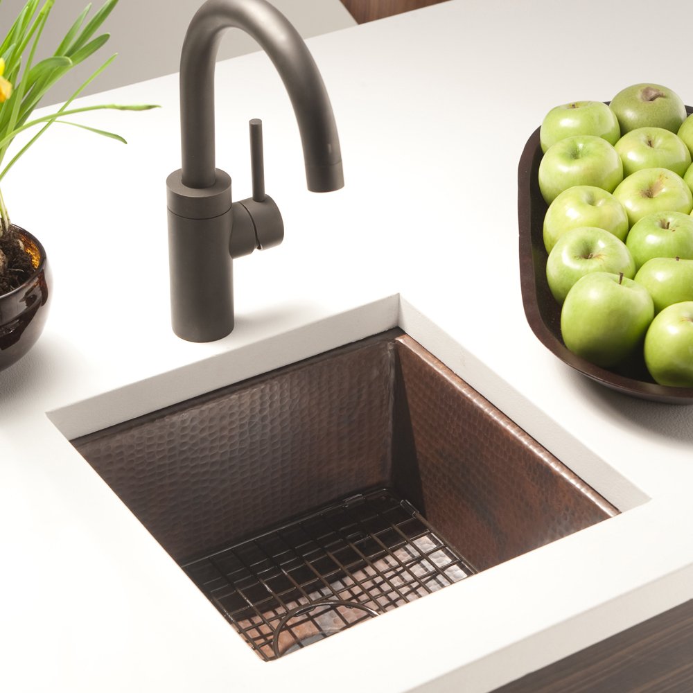 Hammered copper square prep sink with dark metal faucet, grid strainer, and white countertop surround.