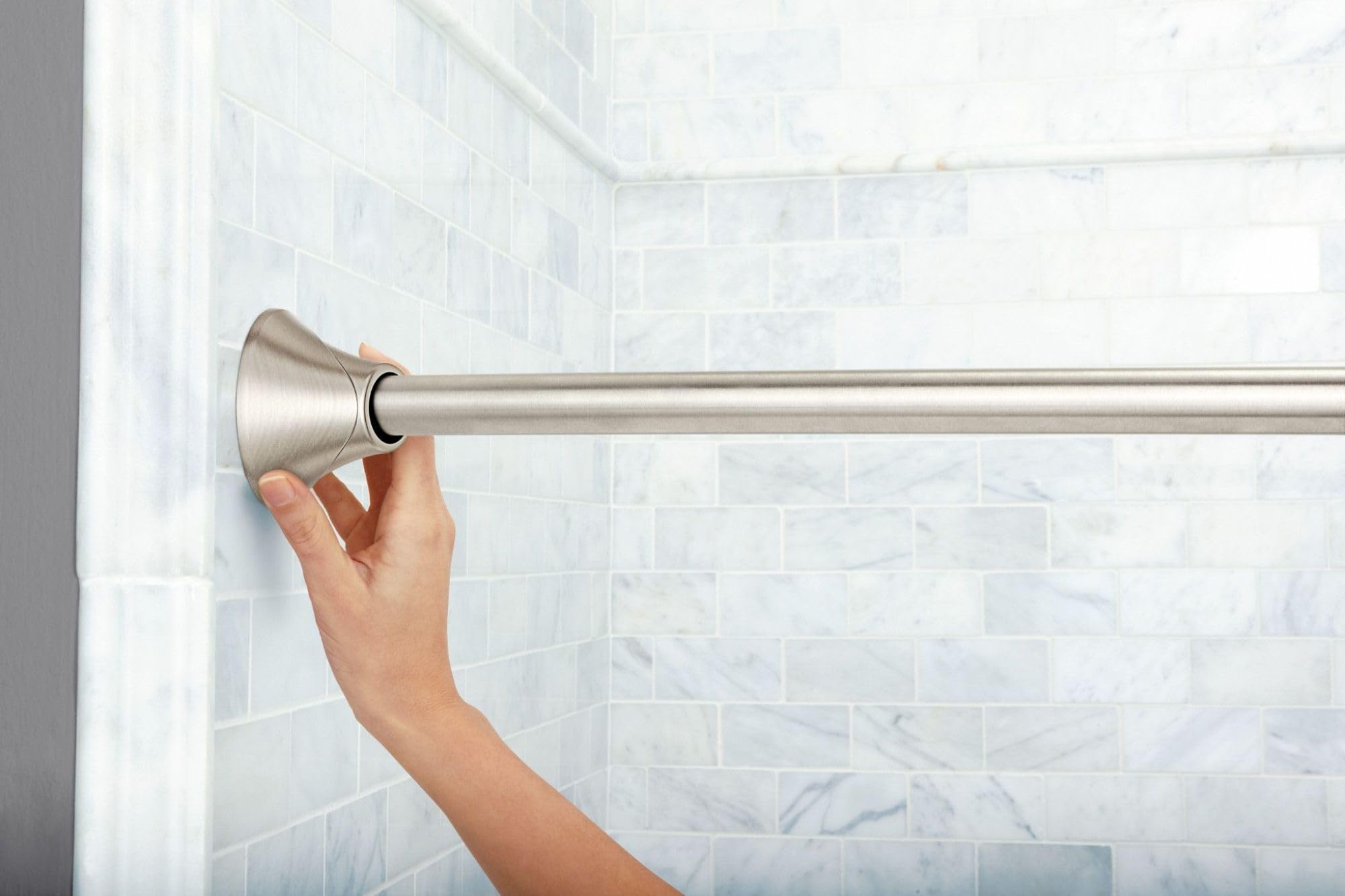 Brushed nickel curved shower curtain rod with cone finial, installed in tiled bathroom.