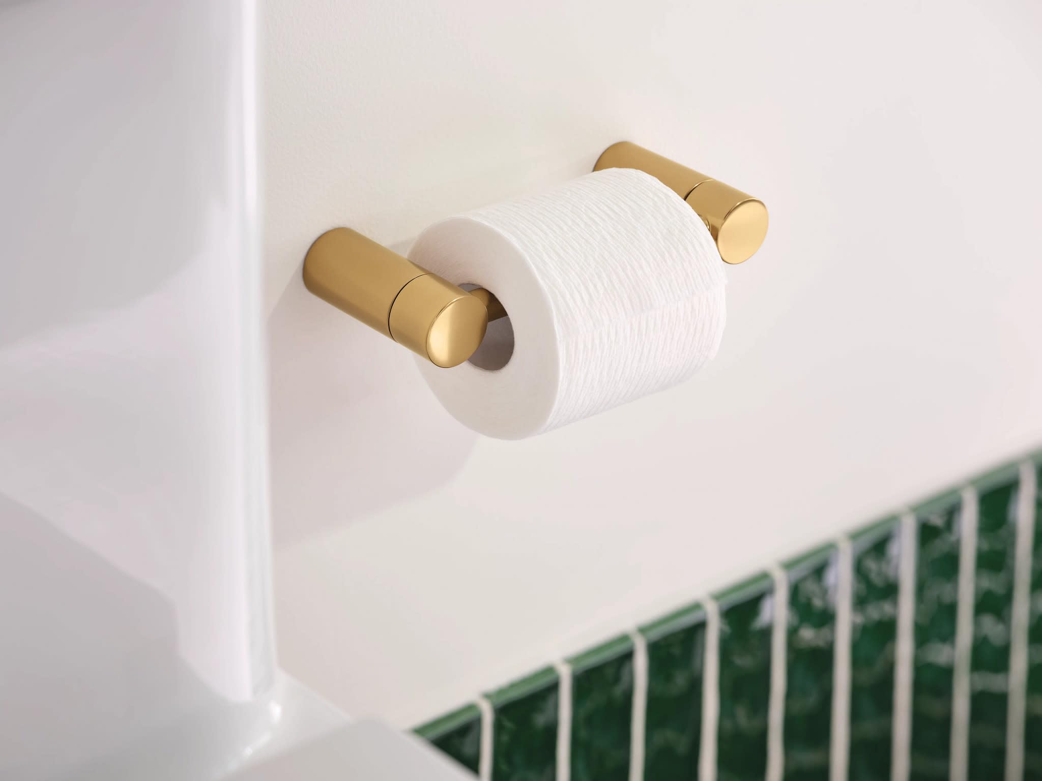 Brushed gold pivoting toilet paper holder mounted on white wall with white toilet paper roll installed.