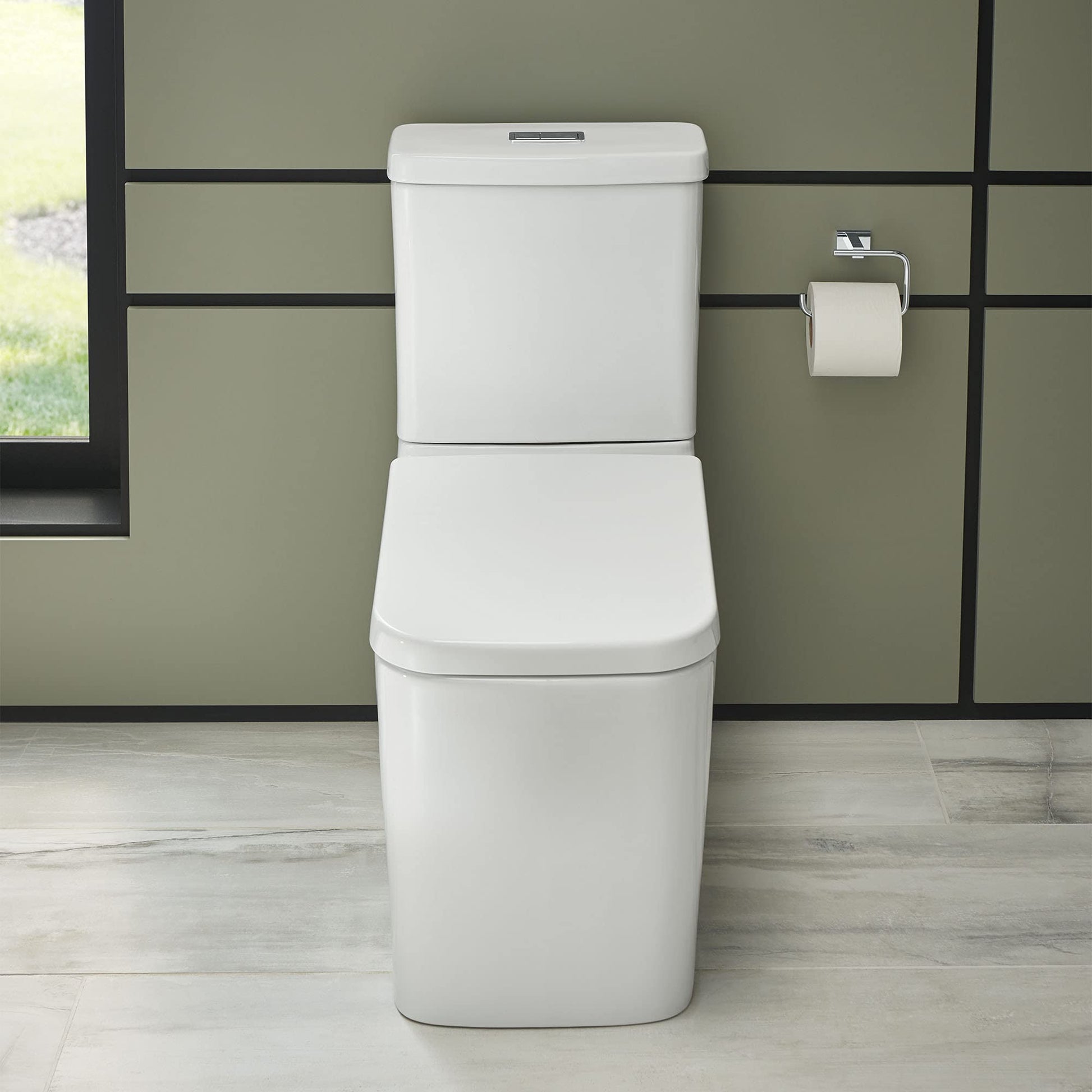 White Grohe Eurocube elongated toilet bowl with tank and seat in bathroom setting against olive green tile wall.