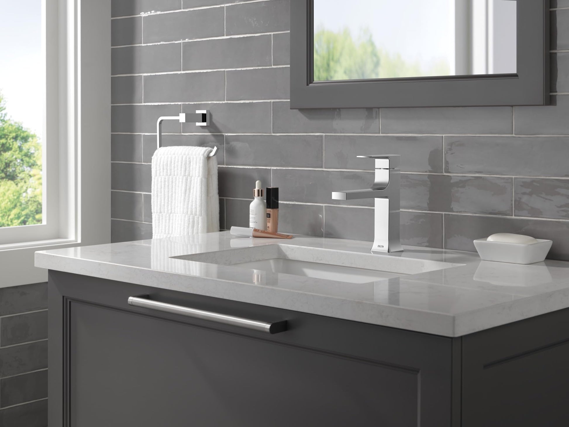 Chrome towel ring mounted on gray subway tile wall above bathroom sink vanity.