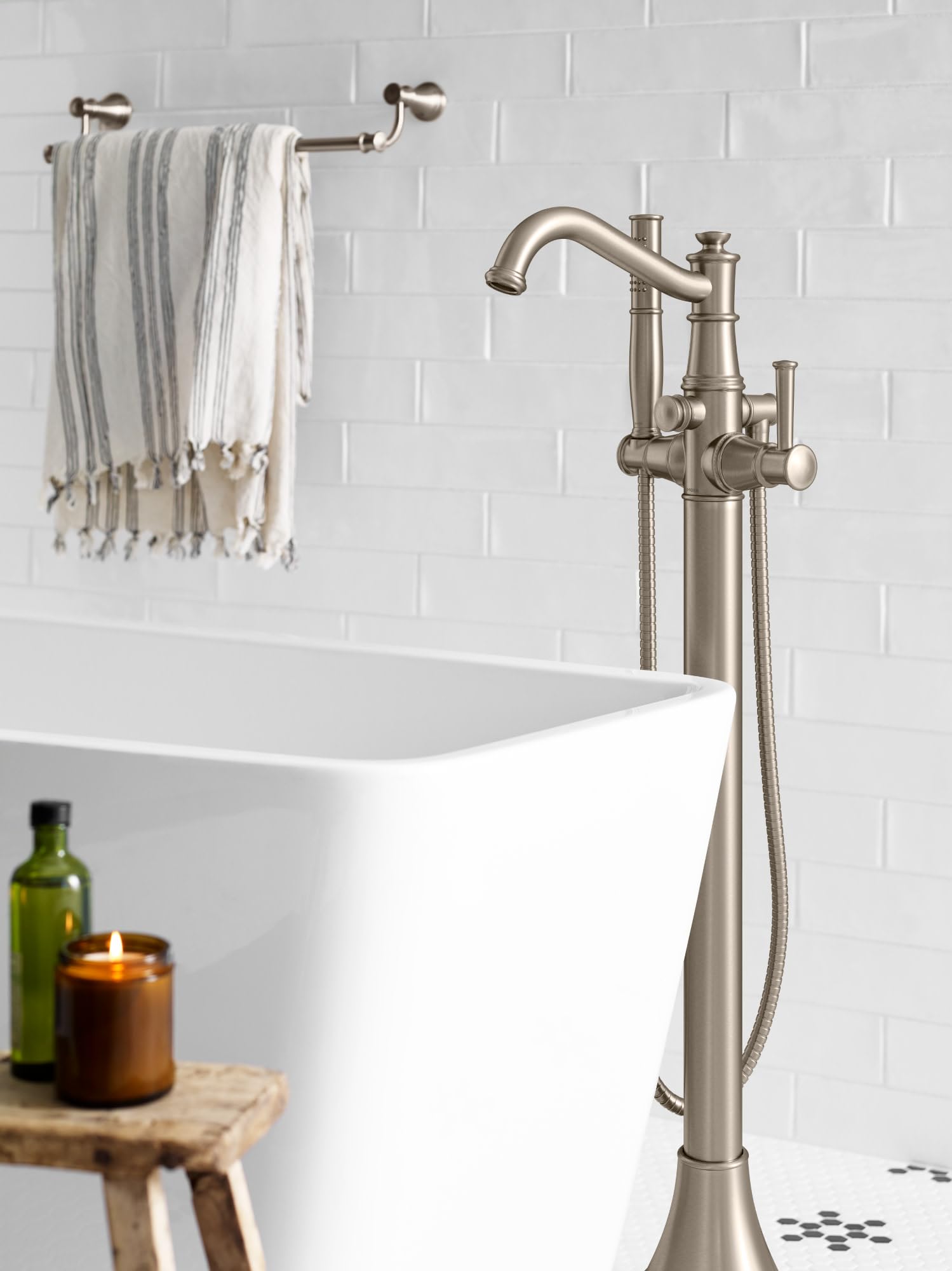 Chrome floor-mounted tub filler with curved spout, single handle, and attached handshower hose next to white freestanding bat