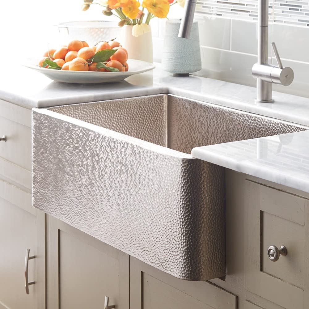 Brushed nickel farmhouse sink with hammered copper interior and single basin mounted in white kitchen countertop.