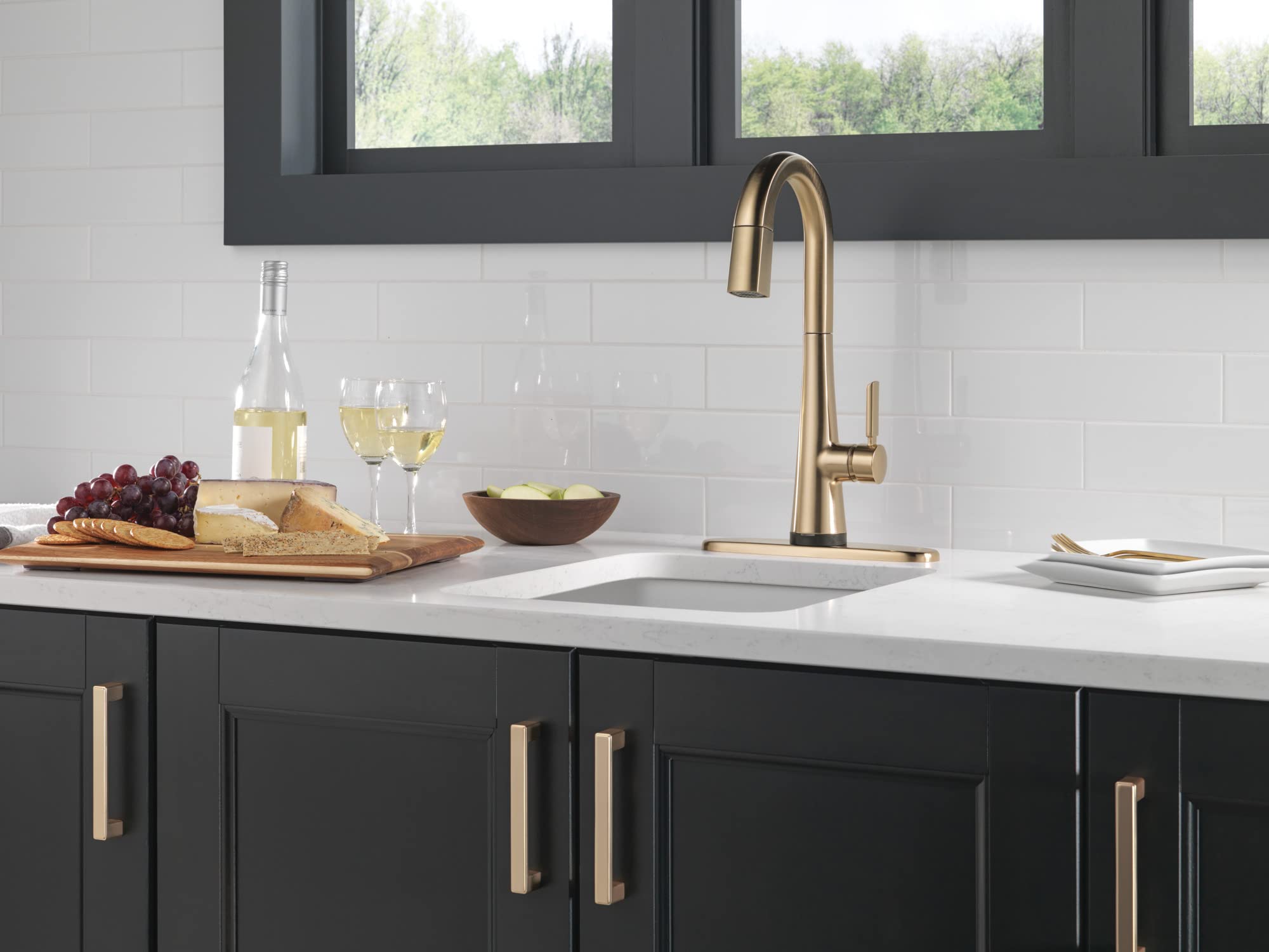 Champagne bronze pull-down kitchen faucet with curved spout mounted above white countertop sink.