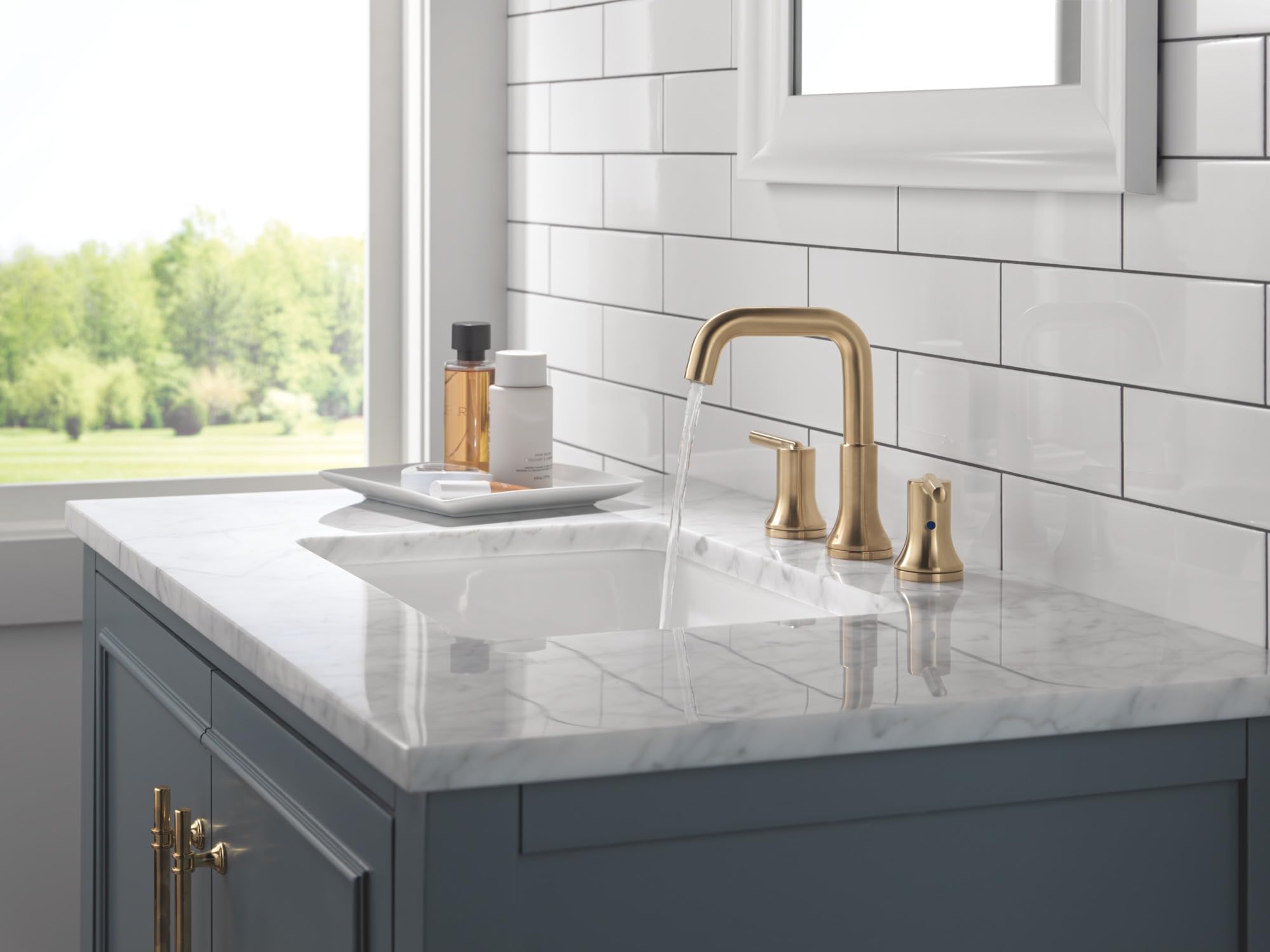 Champagne bronze two-handle widespread bathroom faucet with curved spout installed on marble countertop sink.