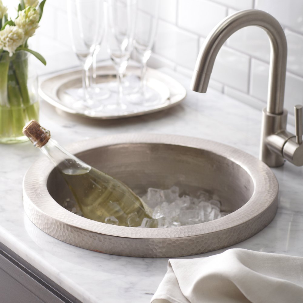Brushed nickel bar sink with hammered finish bowl holding ice and wine bottle, curved faucet, marble countertop.