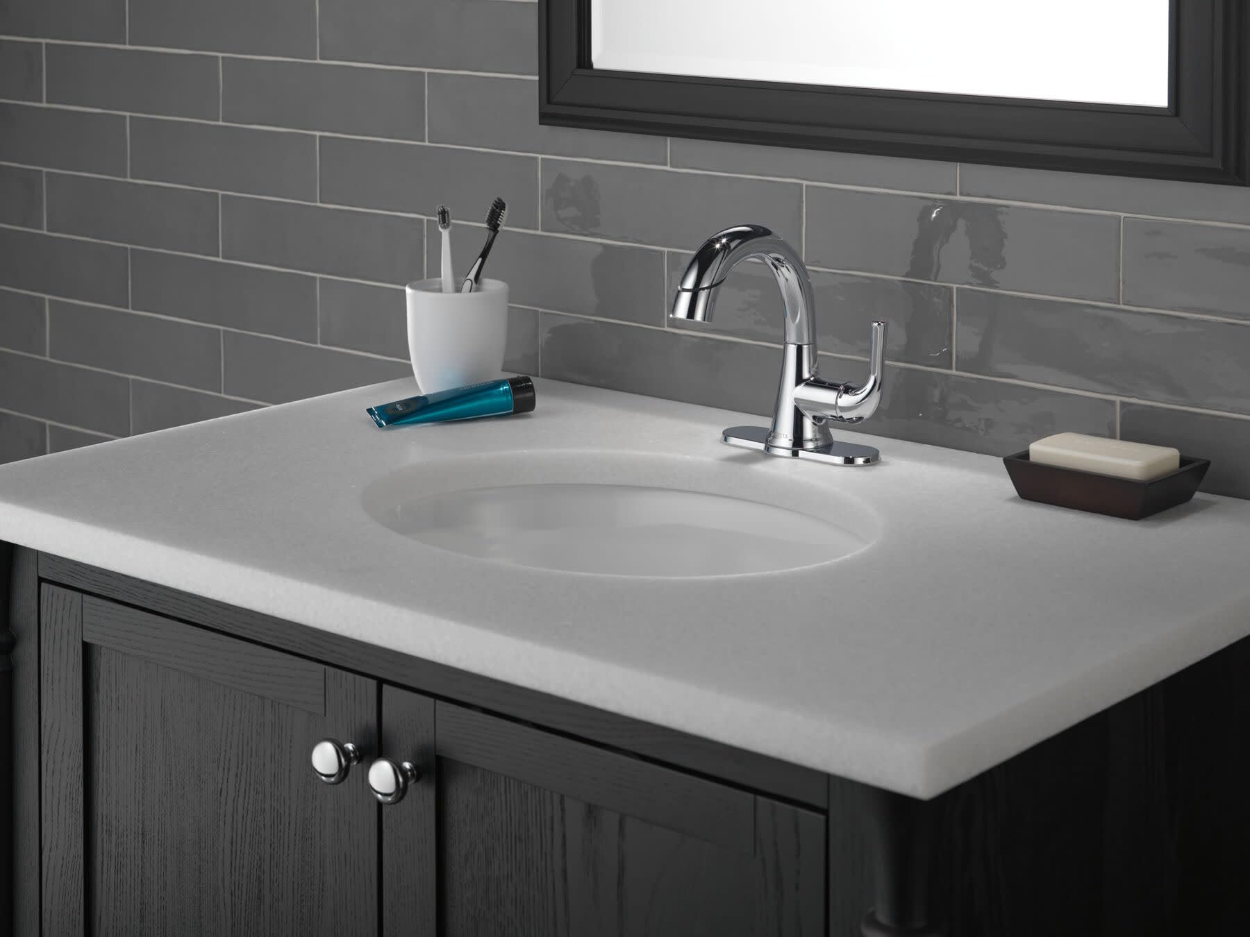 Polished chrome single-handle pull-down faucet mounted on white bathroom vanity with gray tile backsplash.