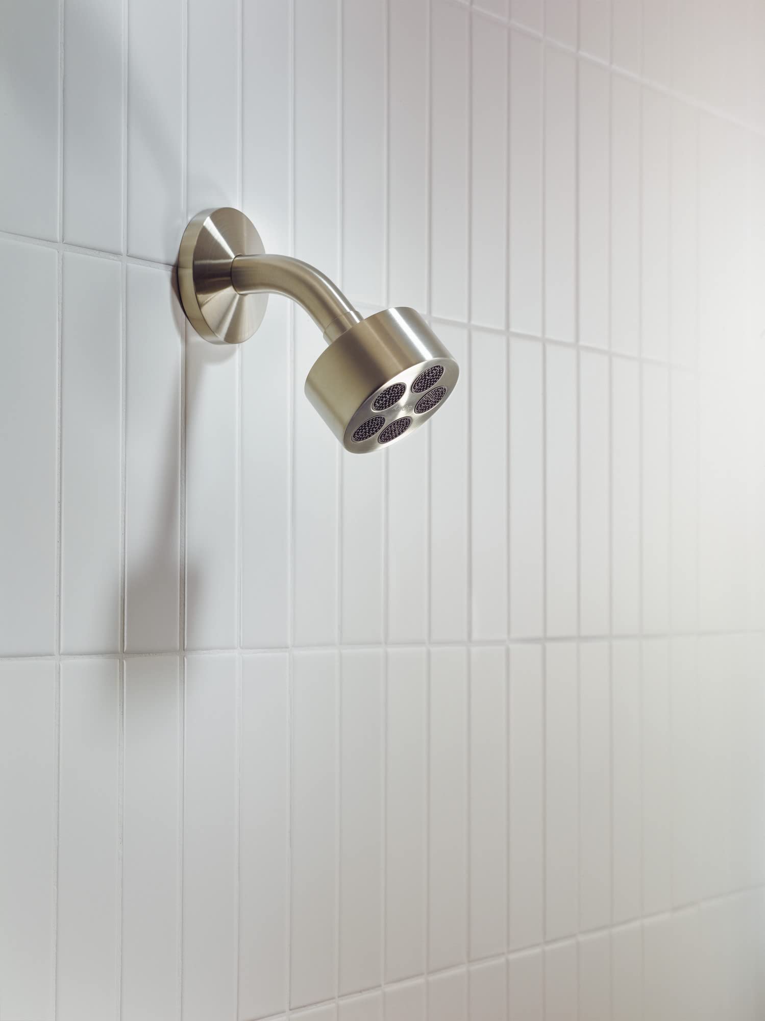 Brushed nickel shower head with curved arm mounted on white subway tile wall.