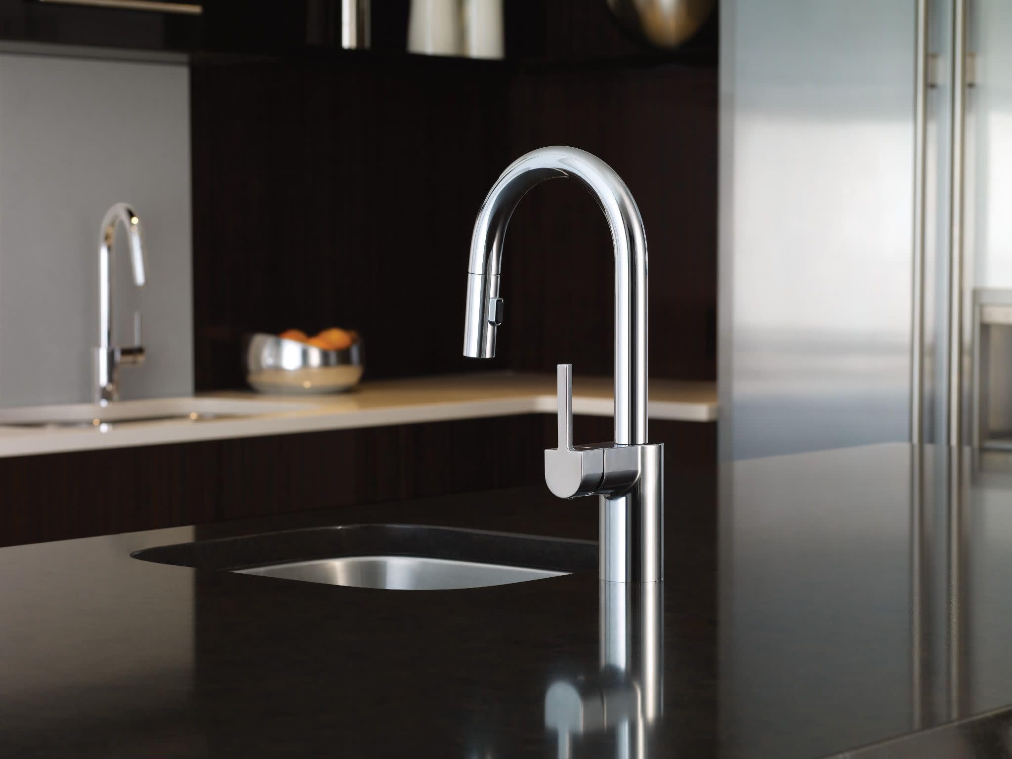 Chrome pulldown kitchen faucet with curved spout and single handle control mounted on black countertop.