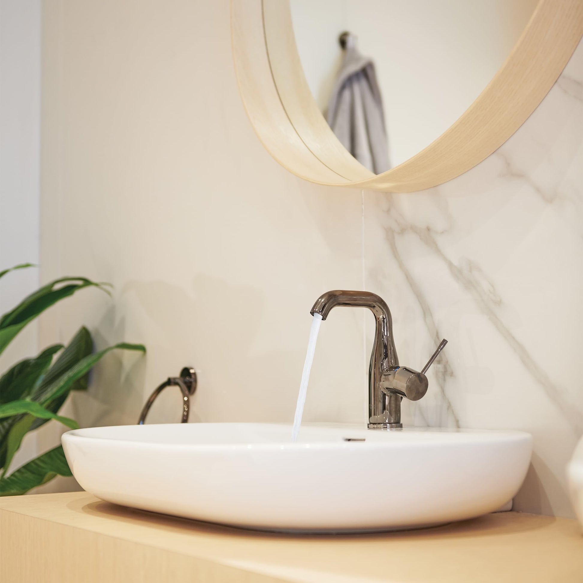 Graphite single-handle bathroom faucet with curved spout mounted above white round sink on wooden countertop.