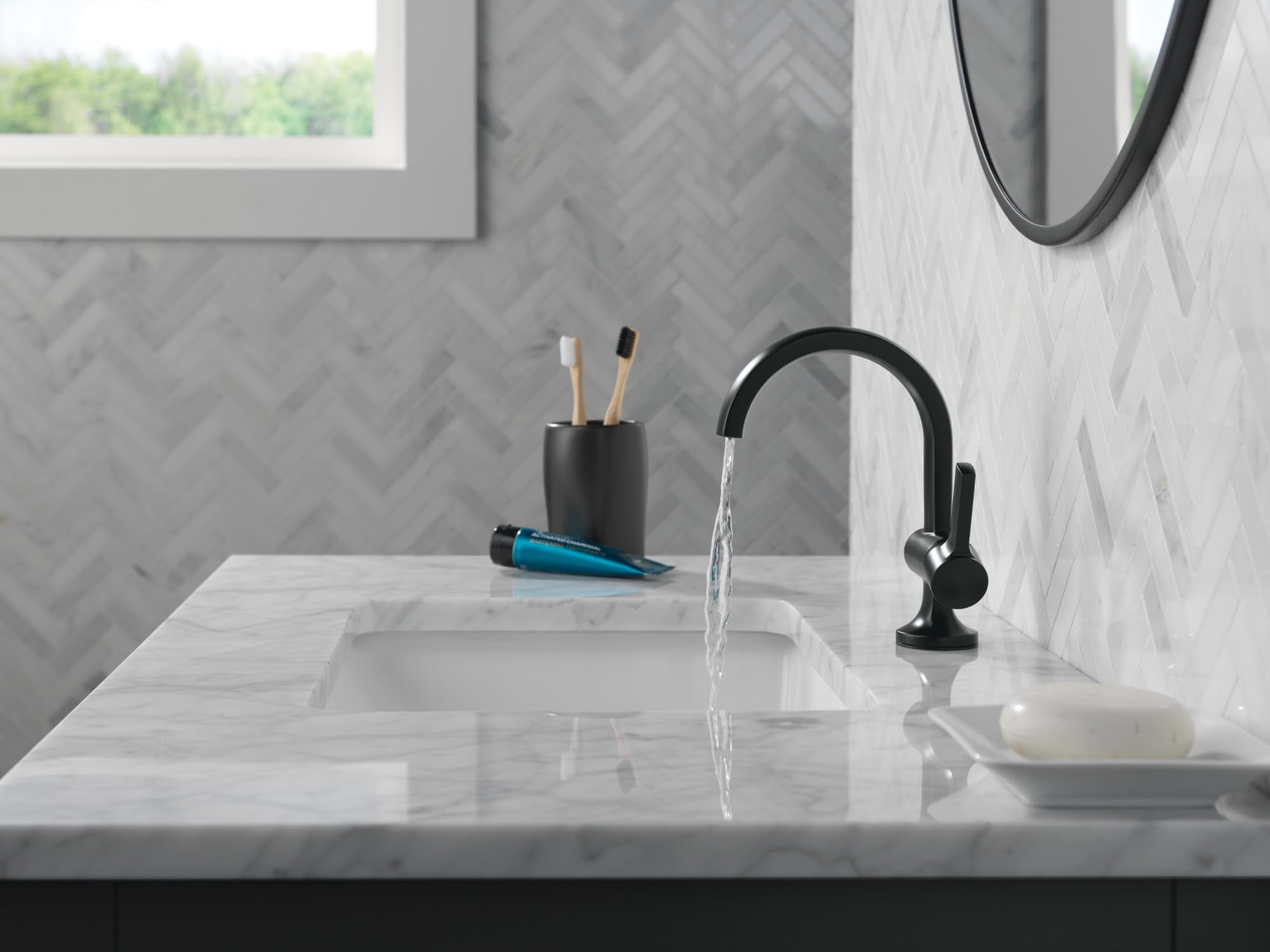 Matte black single-handle bathroom faucet with curved spout installed on marble countertop, water running.