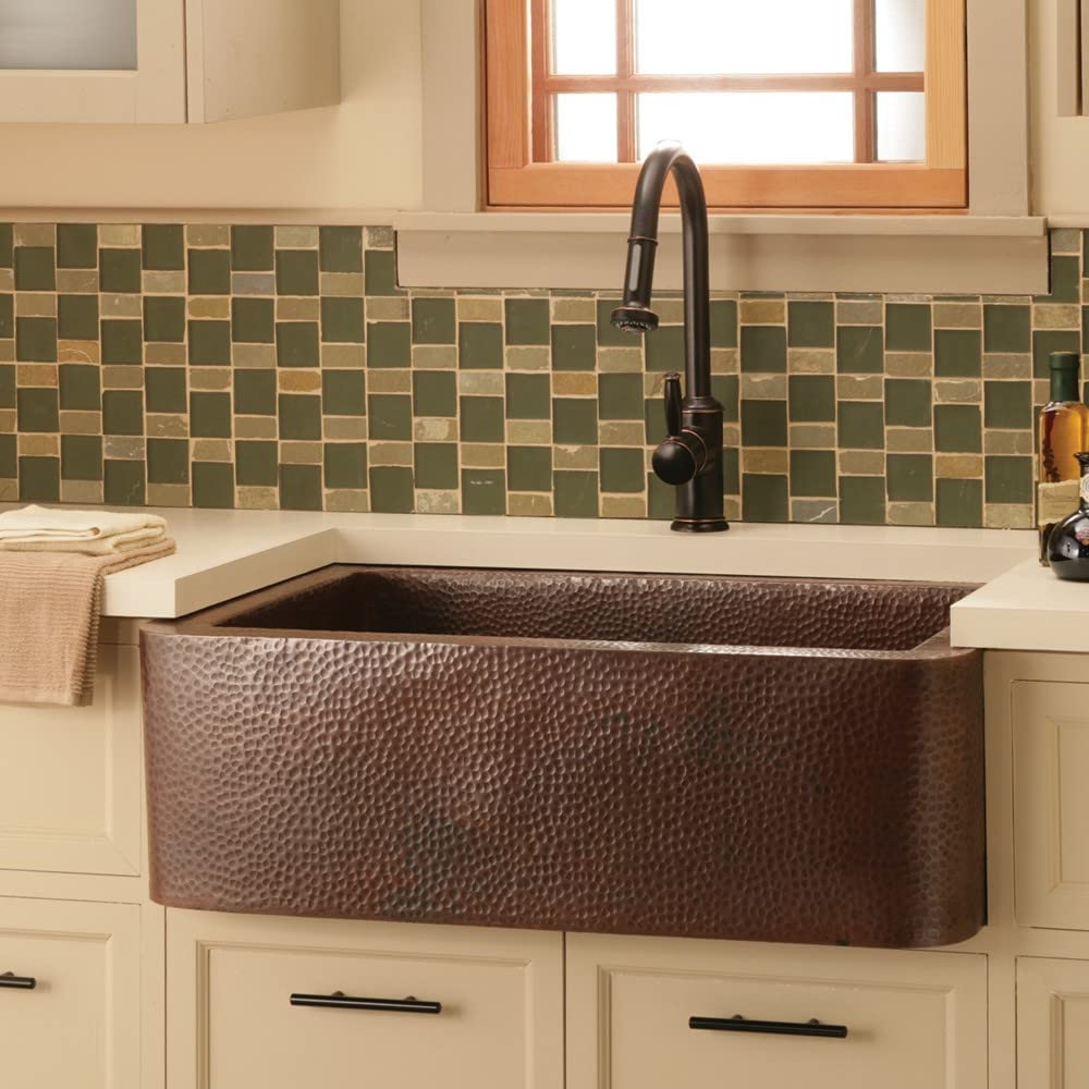 Antique copper farmhouse sink with hammered texture and curved apron front installed in cream cabinetry.