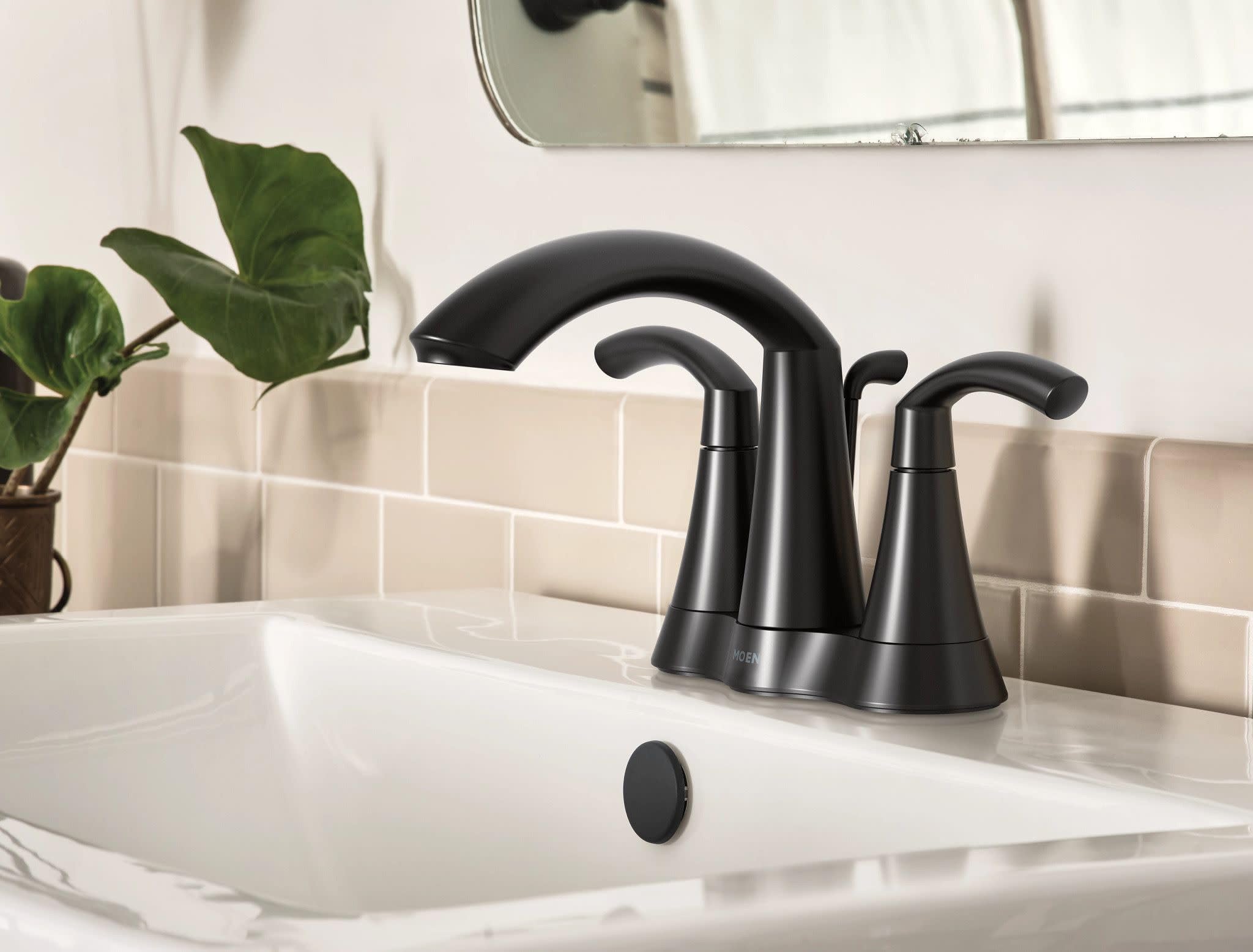 Matte black two-handle bathroom faucet with high arc spout installed on white sink with subway tile backsplash.