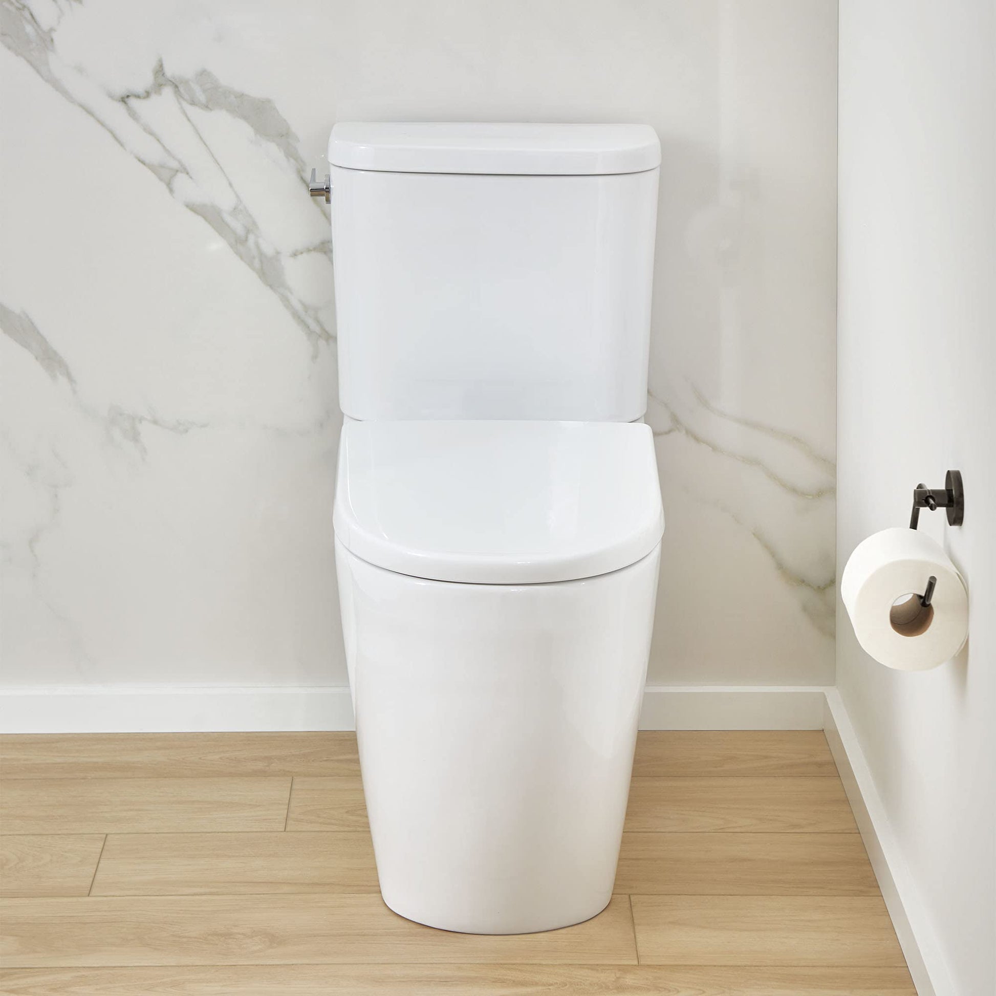 White two-piece elongated toilet with seat and left-hand trip lever installed in bathroom with marble walls.