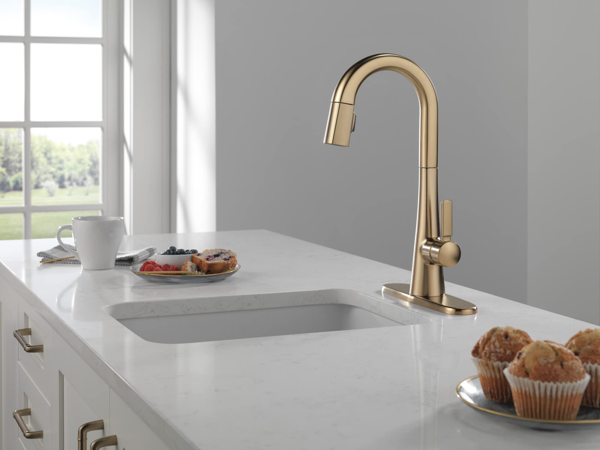 Champagne bronze kitchen faucet with curved spout and pull-down spray head on white countertop.