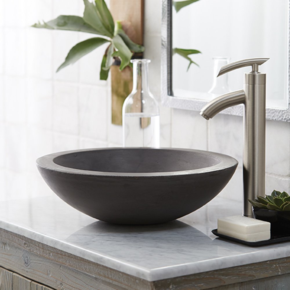 Dark slate vessel sink with rounded bowl shape on marble countertop next to stainless steel faucet.