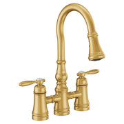 Brushed gold bridge kitchen faucet with two handles, curved pulldown spout, and tapered body with decorative rings.