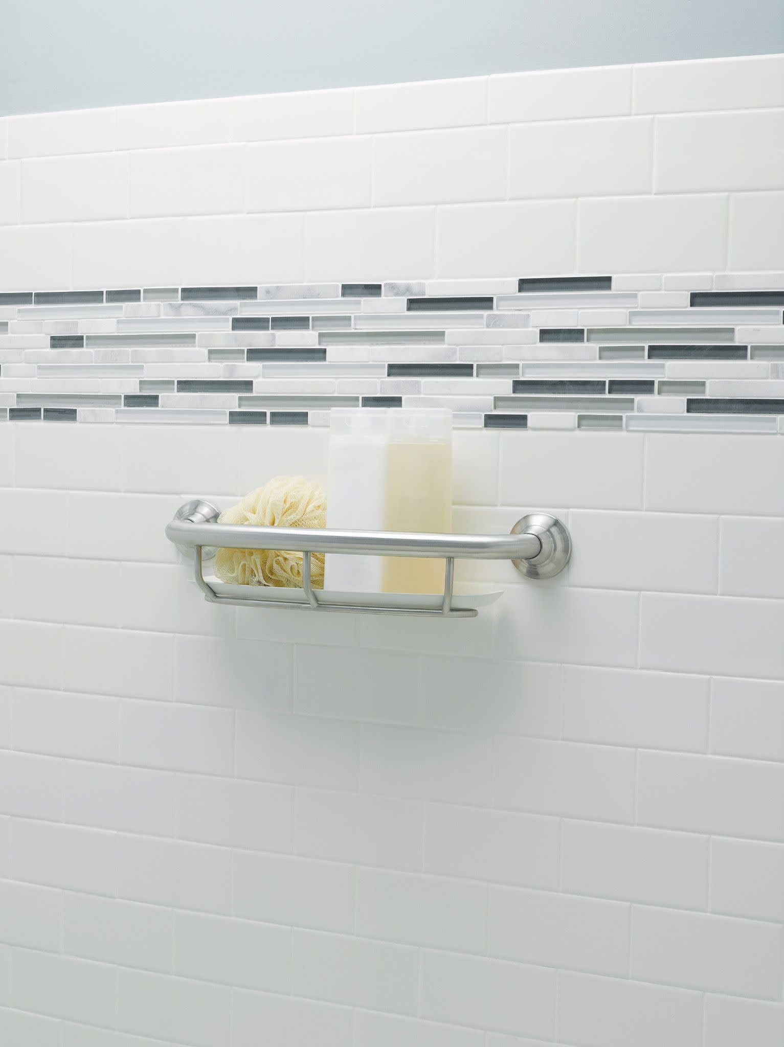 Brushed nickel grab bar with shelf mounted on white subway tile wall, holding a loofah and soap bottle.