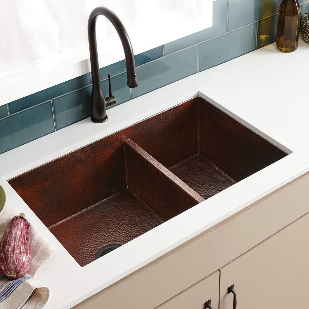 Double-basin undermount copper kitchen sink with hammered interior finish and black gooseneck faucet installed in white count