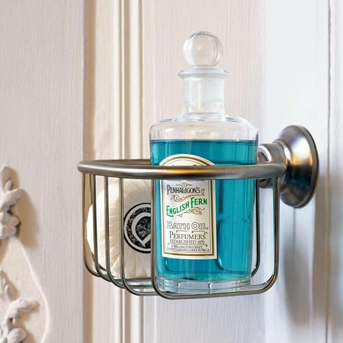 Brushed nickel rectangular shower basket with rounded corners holding a glass bottle of bath oil against a white textured wal