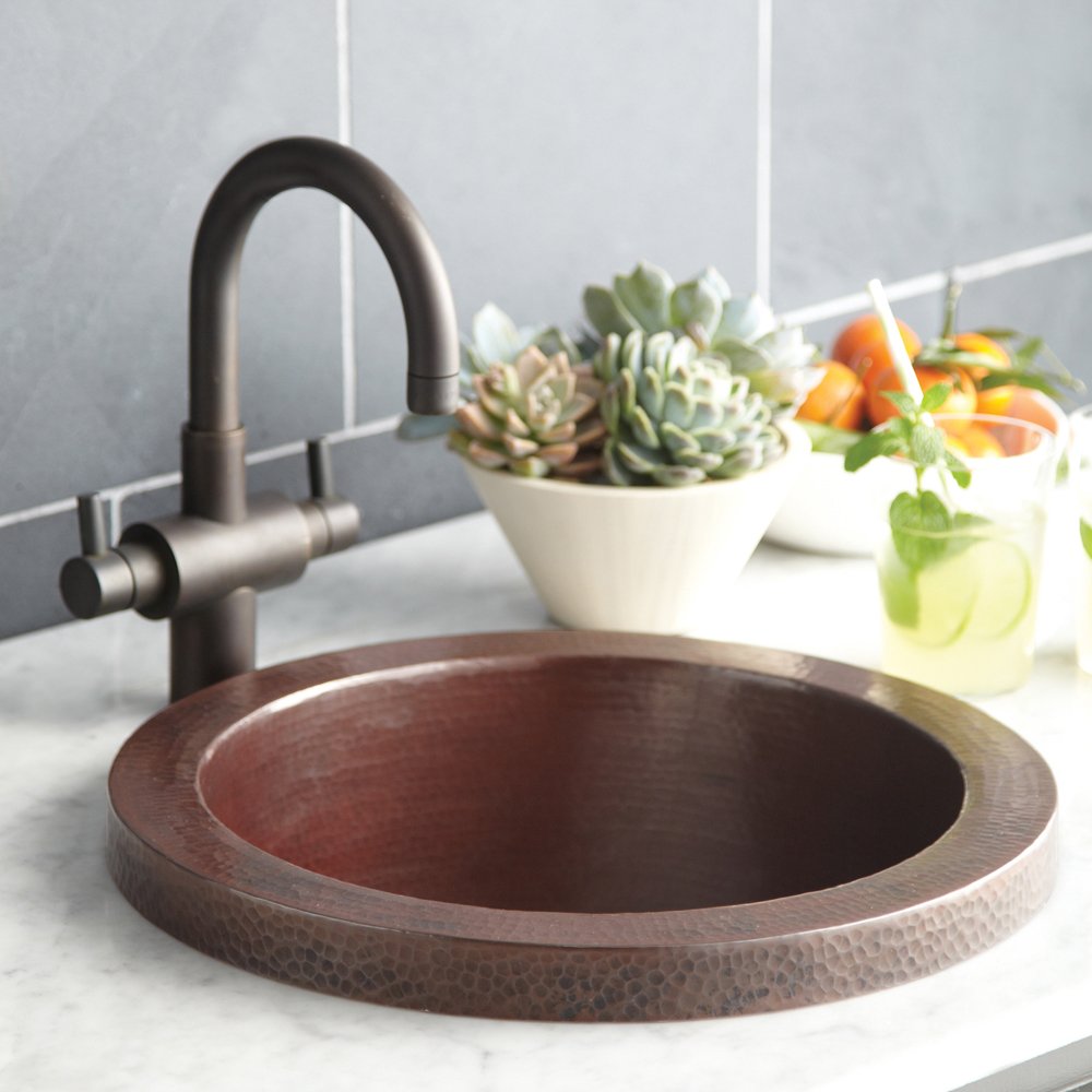 Antique copper round bar sink with dark arched faucet on marble countertop.