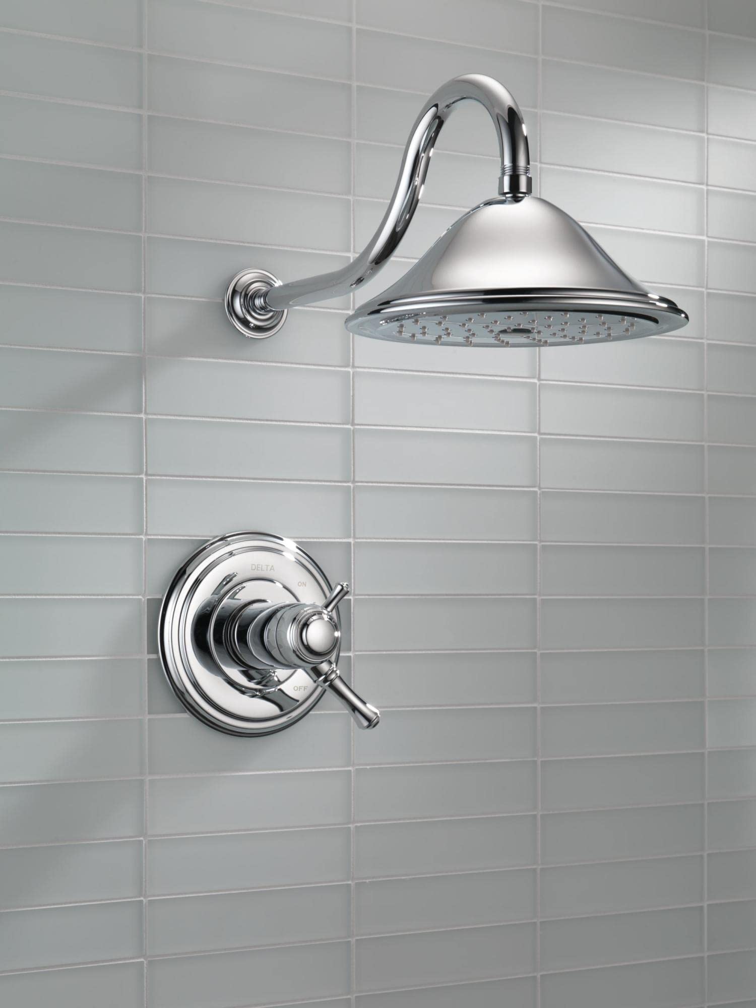 Chrome shower trim with dome showerhead and curved arm mounted on wall with control valve below.