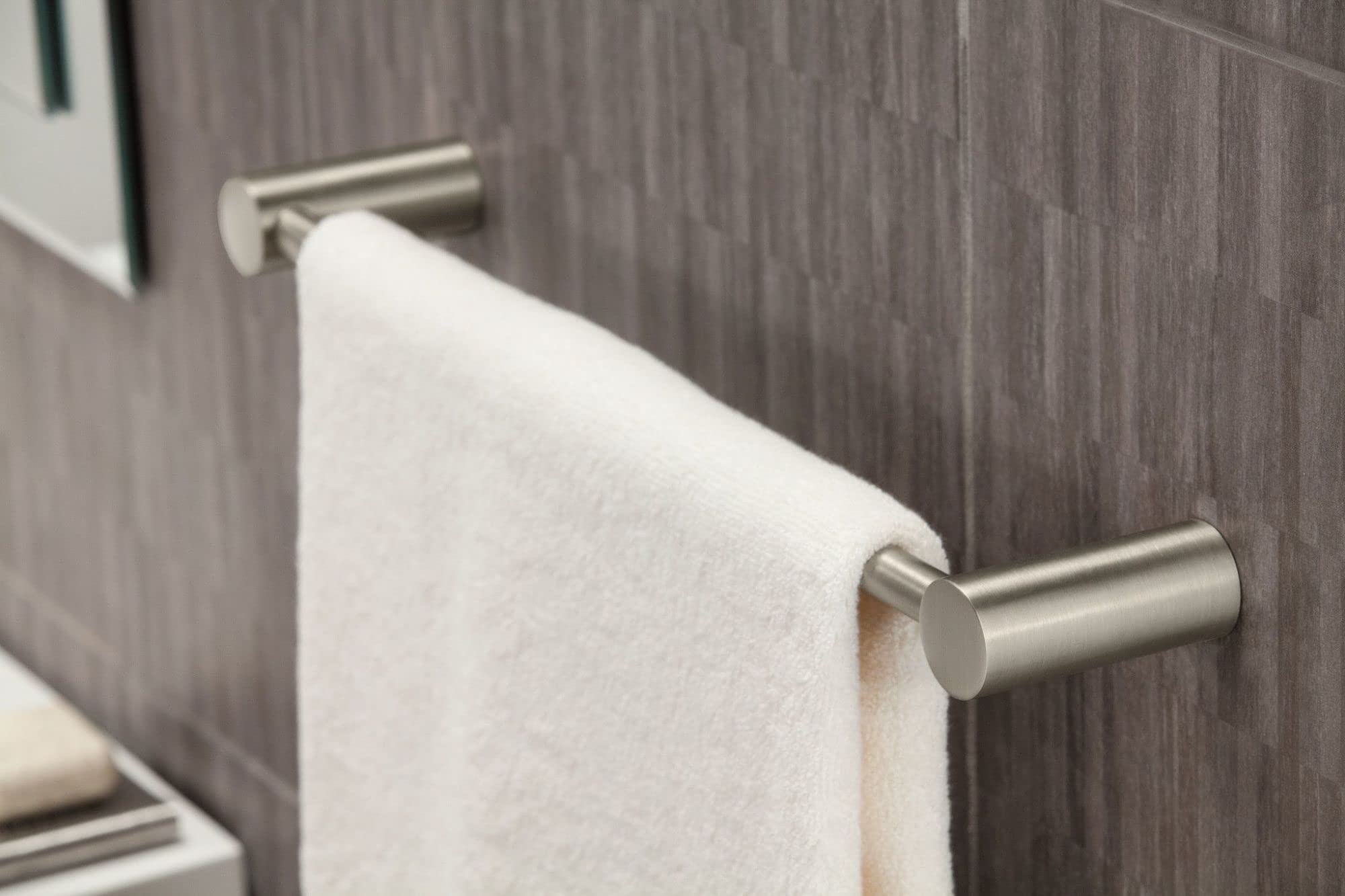 Brushed nickel wall-mounted towel bar with white towel draped over cylindrical rod on tiled bathroom wall.
