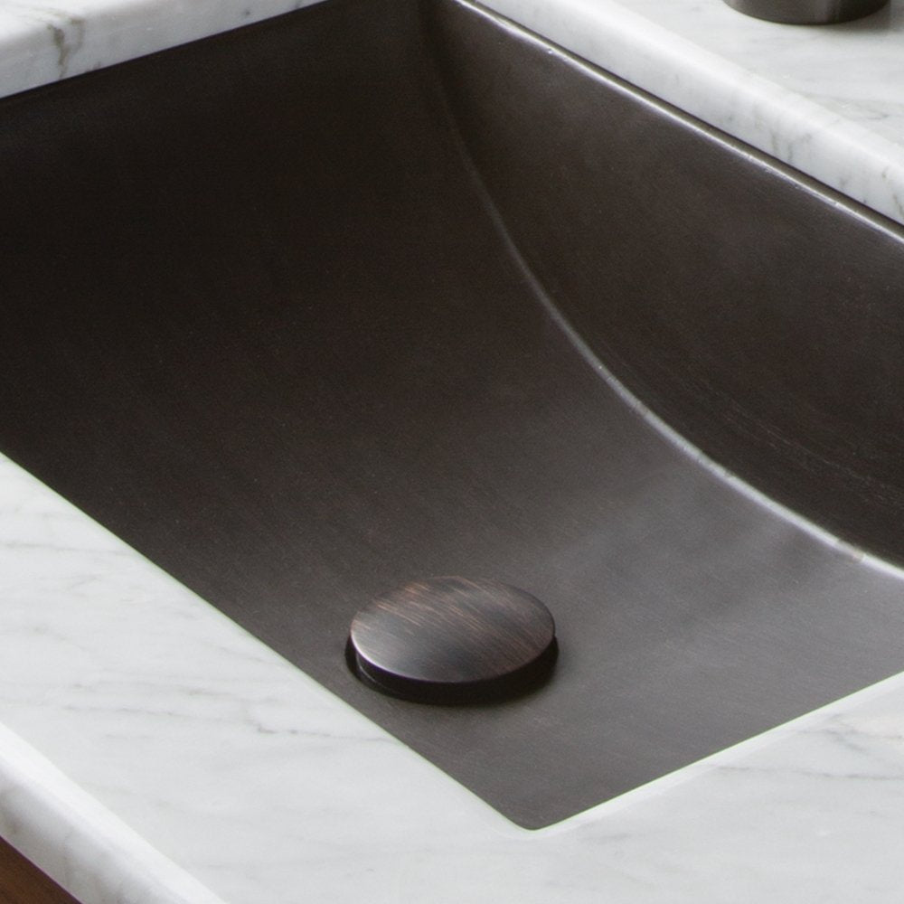 Weathered copper push-to-seal dome drain installed in dark sink basin with marble countertop.