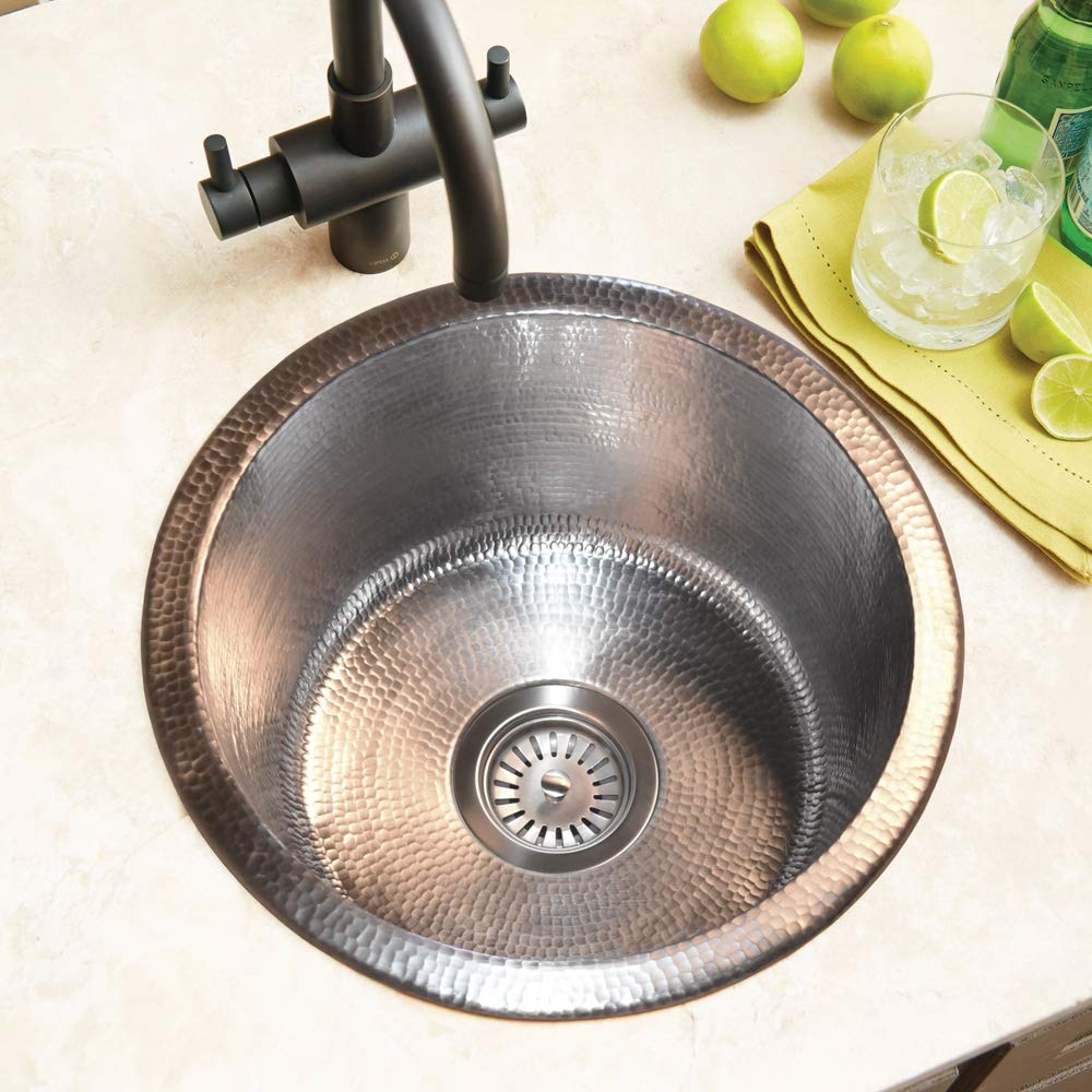 Hammered copper round bar sink with drain and black faucet mounted on countertop.