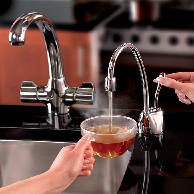 Chrome instant hot water dispenser faucet dispensing hot water into a glass cup held by a hand.