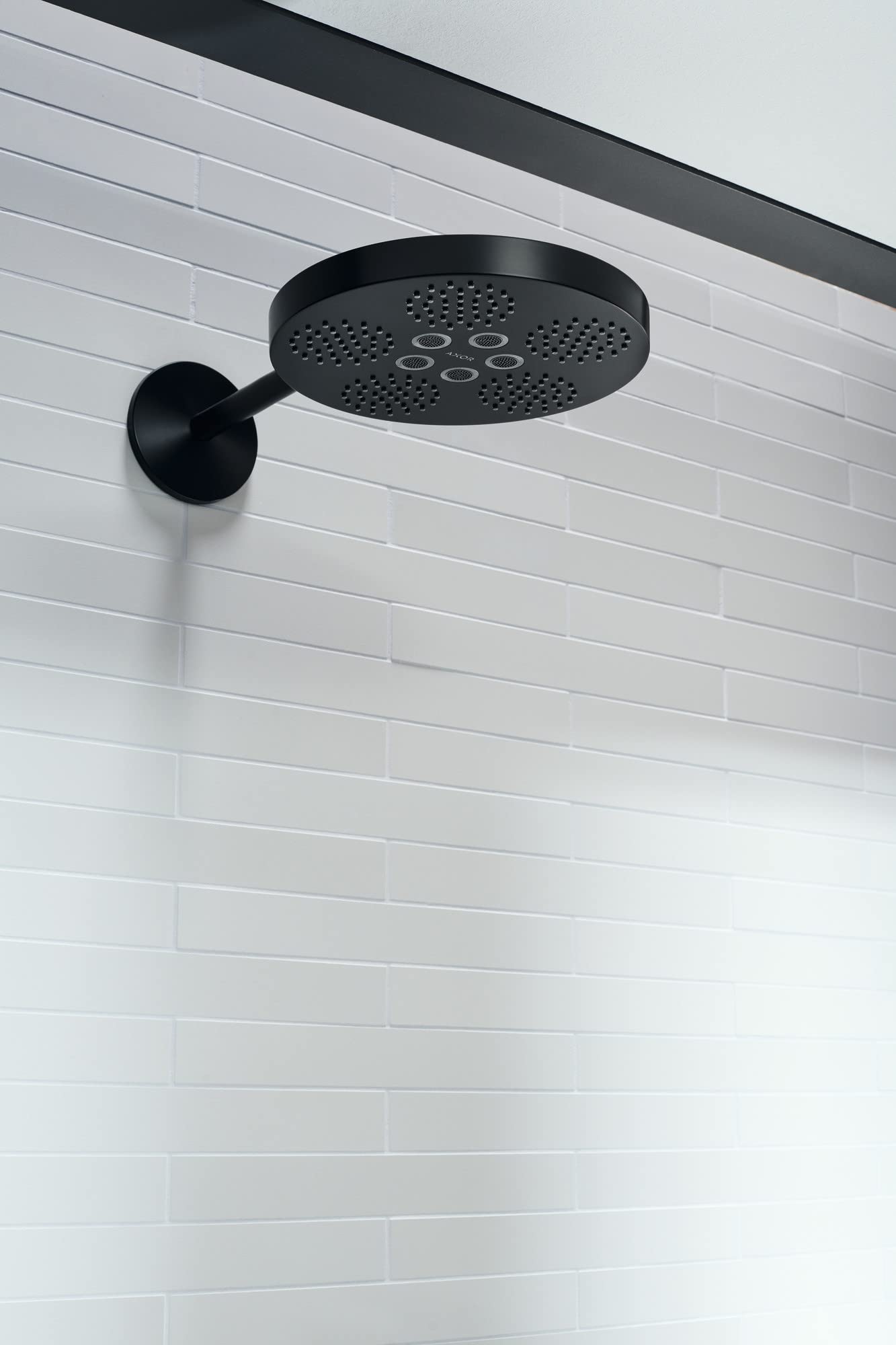 Matte black round shower head with perforated face mounted on white subway tile wall via curved arm.