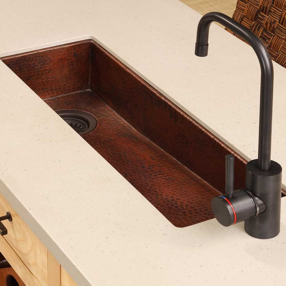 Hammered copper bar sink with dark patina finish and black gooseneck faucet installed in countertop.