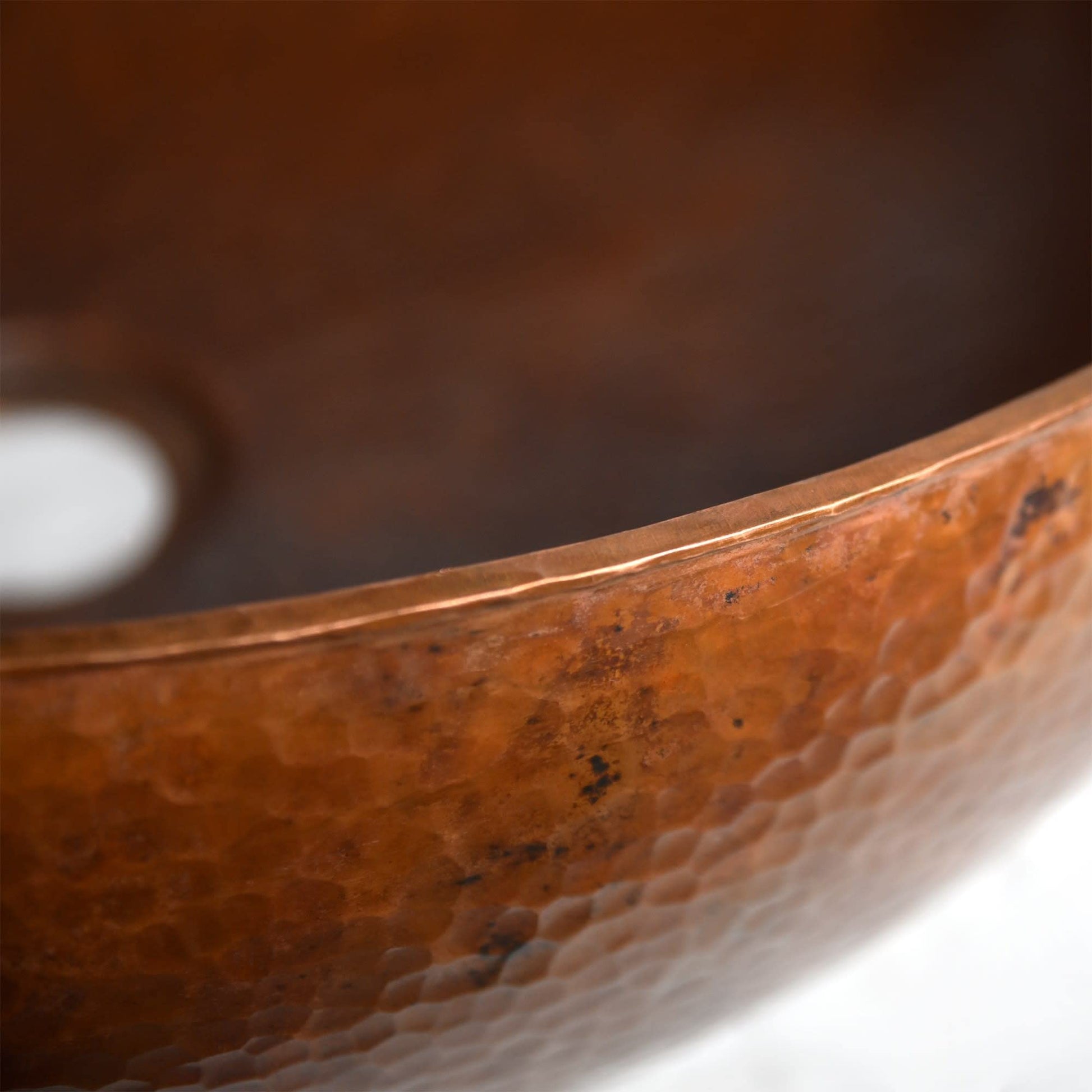 Hammered copper vessel sink with textured surface and polished rim, shown in close-up detail.