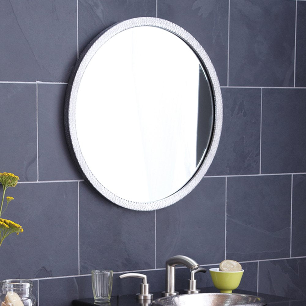 Round wall mirror with white textured frame mounted above bathroom sink and dark tile wall.