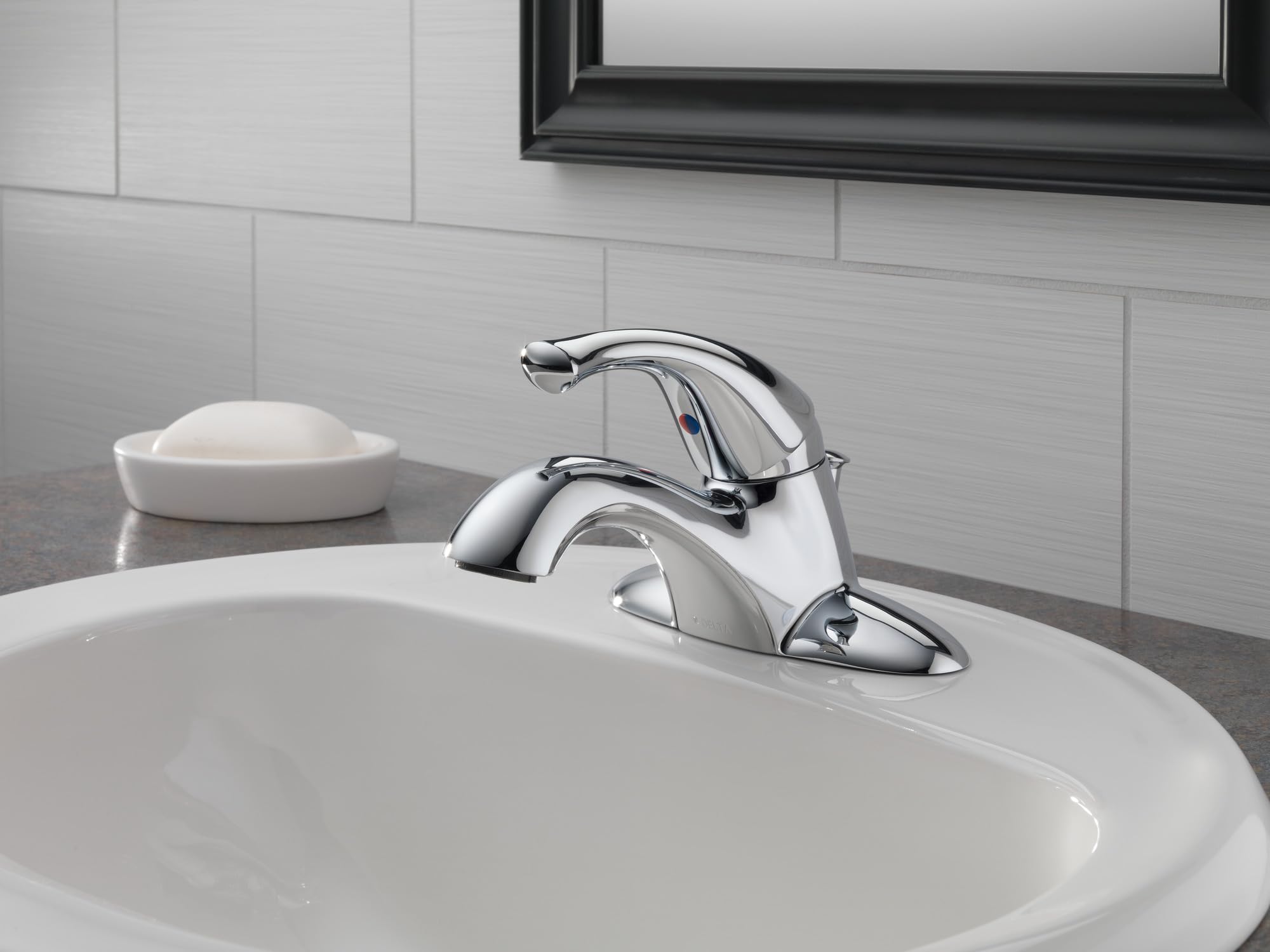 Chrome single-handle bathroom faucet with curved spout mounted on white sink with subway tile backsplash.