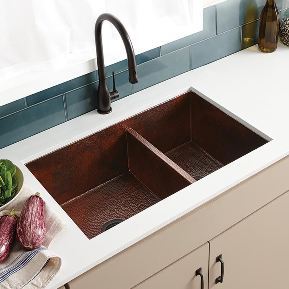 Antique copper double-basin undermount kitchen sink with hammered finish and black pull-down faucet installed in white counte