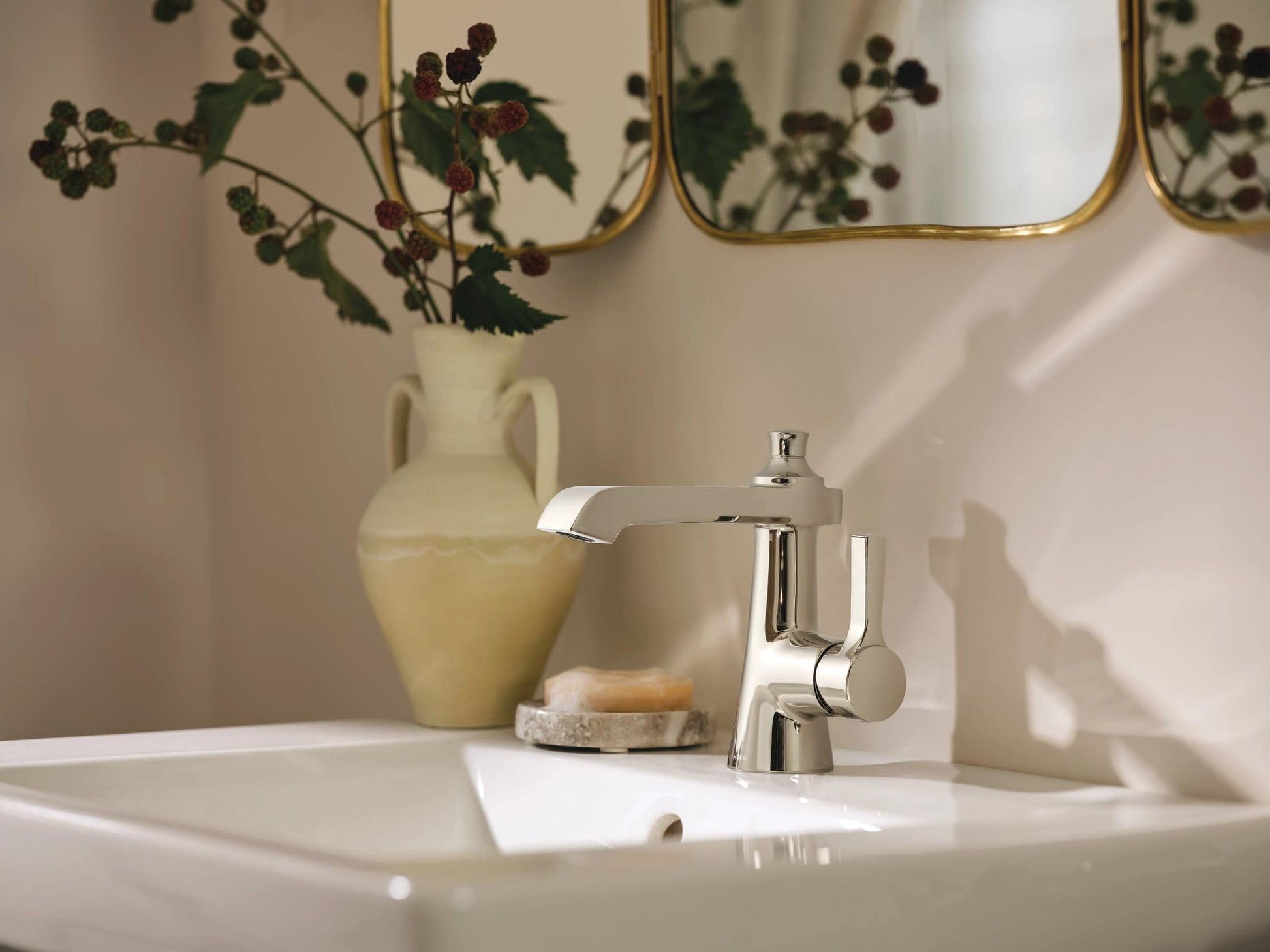 Polished nickel single-handle bathroom sink faucet with curved spout mounted on white sink countertop.