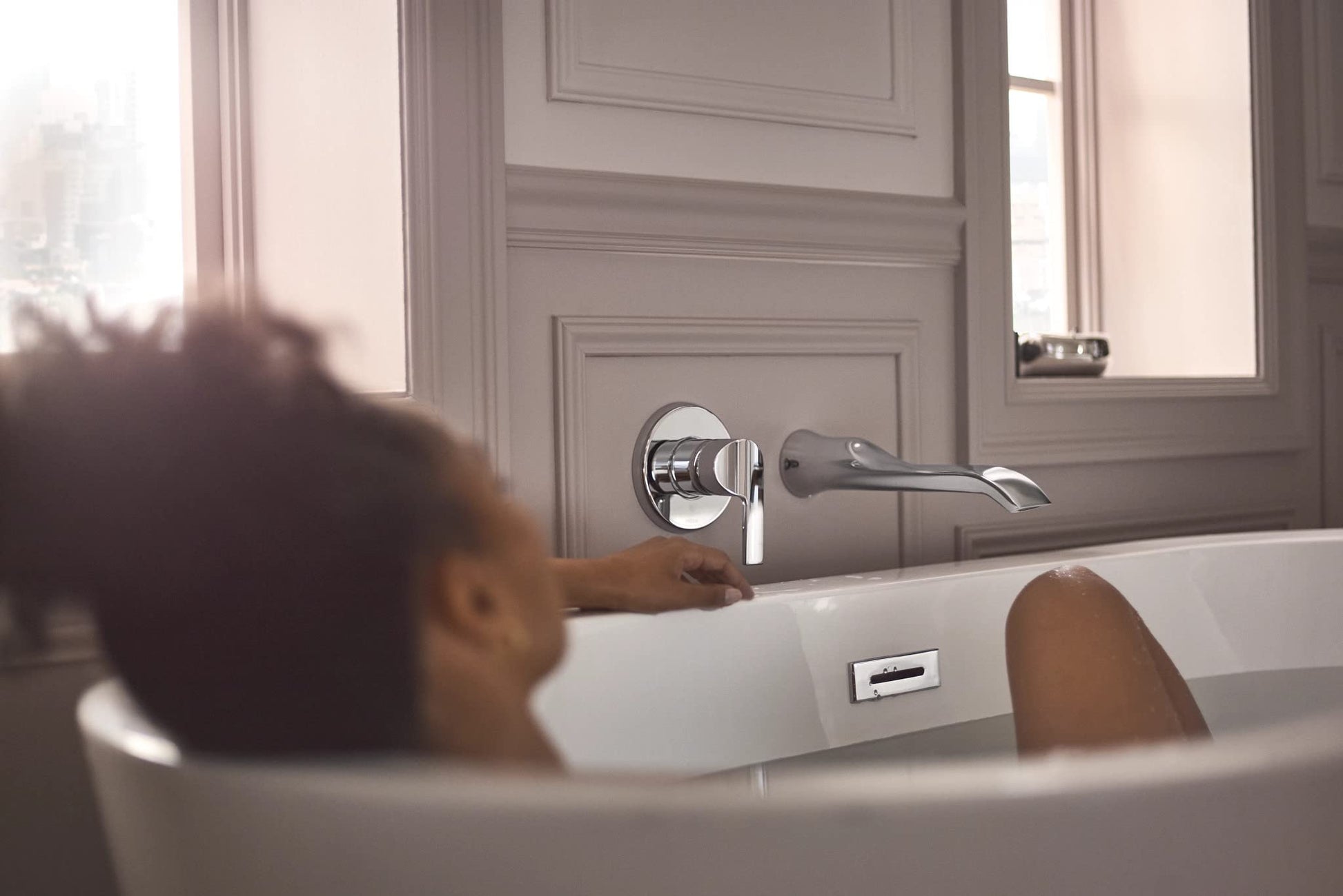Chrome wall-mounted tub faucet with single handle and curved spout installed above bathtub.