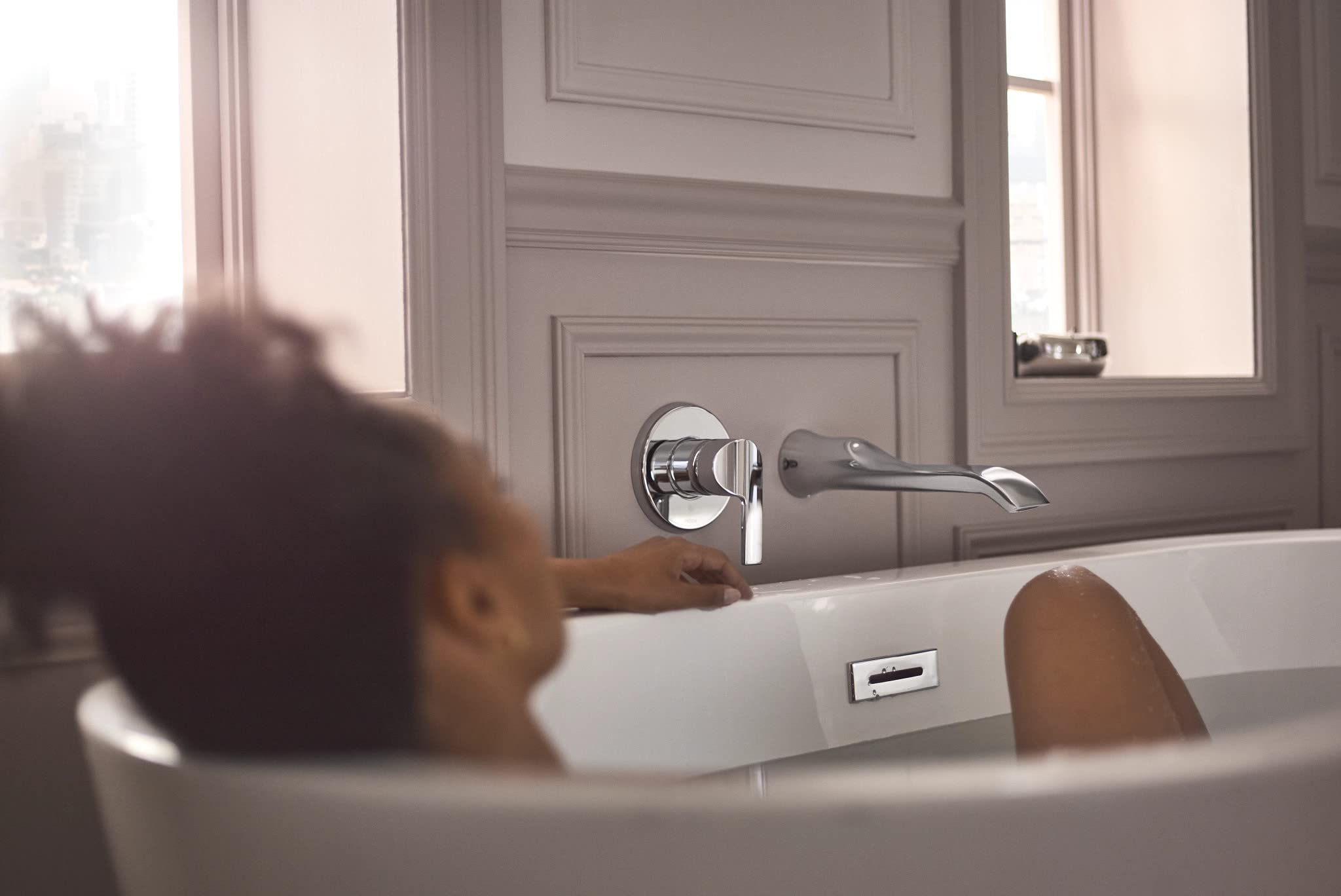 Chrome wall-mounted tub faucet with single handle and curved spout installed above bathtub.