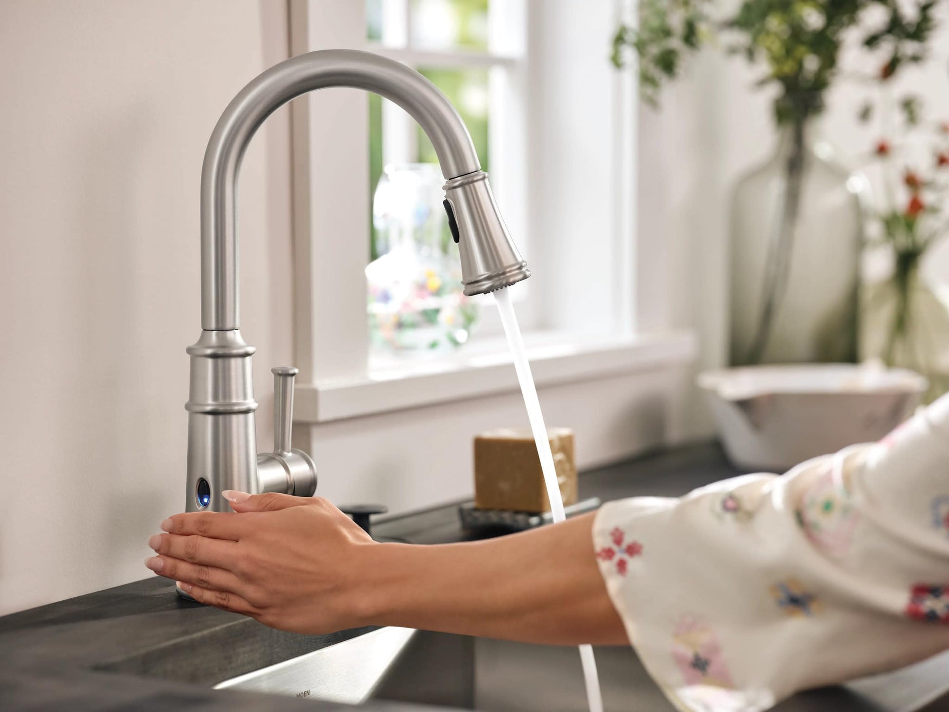 Stainless steel pulldown kitchen faucet with curved spout and single handle, activated by hand motion near sensor, dispensing