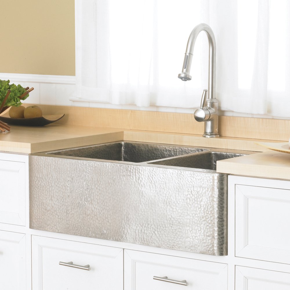 Brushed nickel dual-basin farmhouse sink with hammered copper exterior and pull-down kitchen faucet installed in light wood c