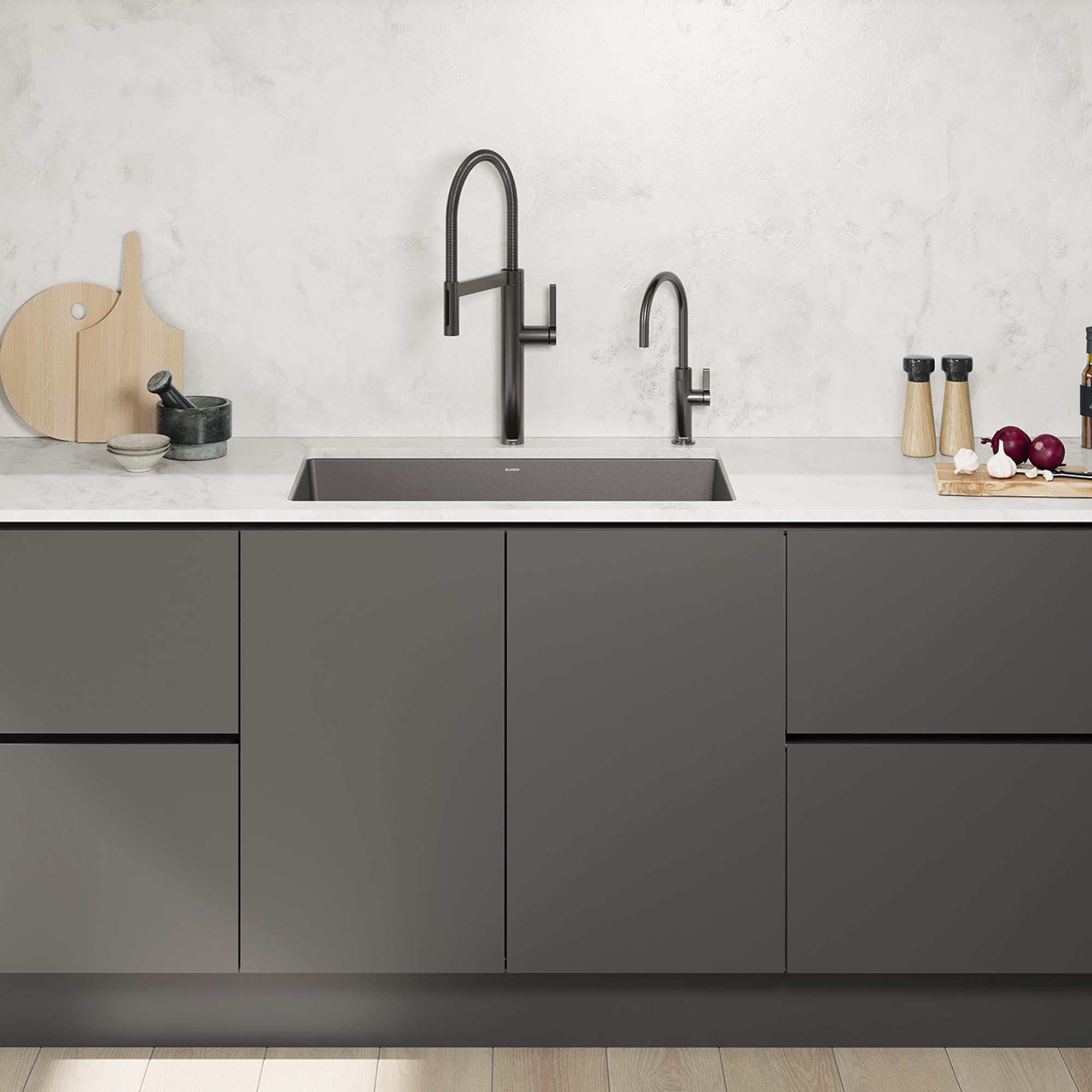 Satin dark steel beverage faucet with curved pull-down spout installed above kitchen sink with marble backsplash.
