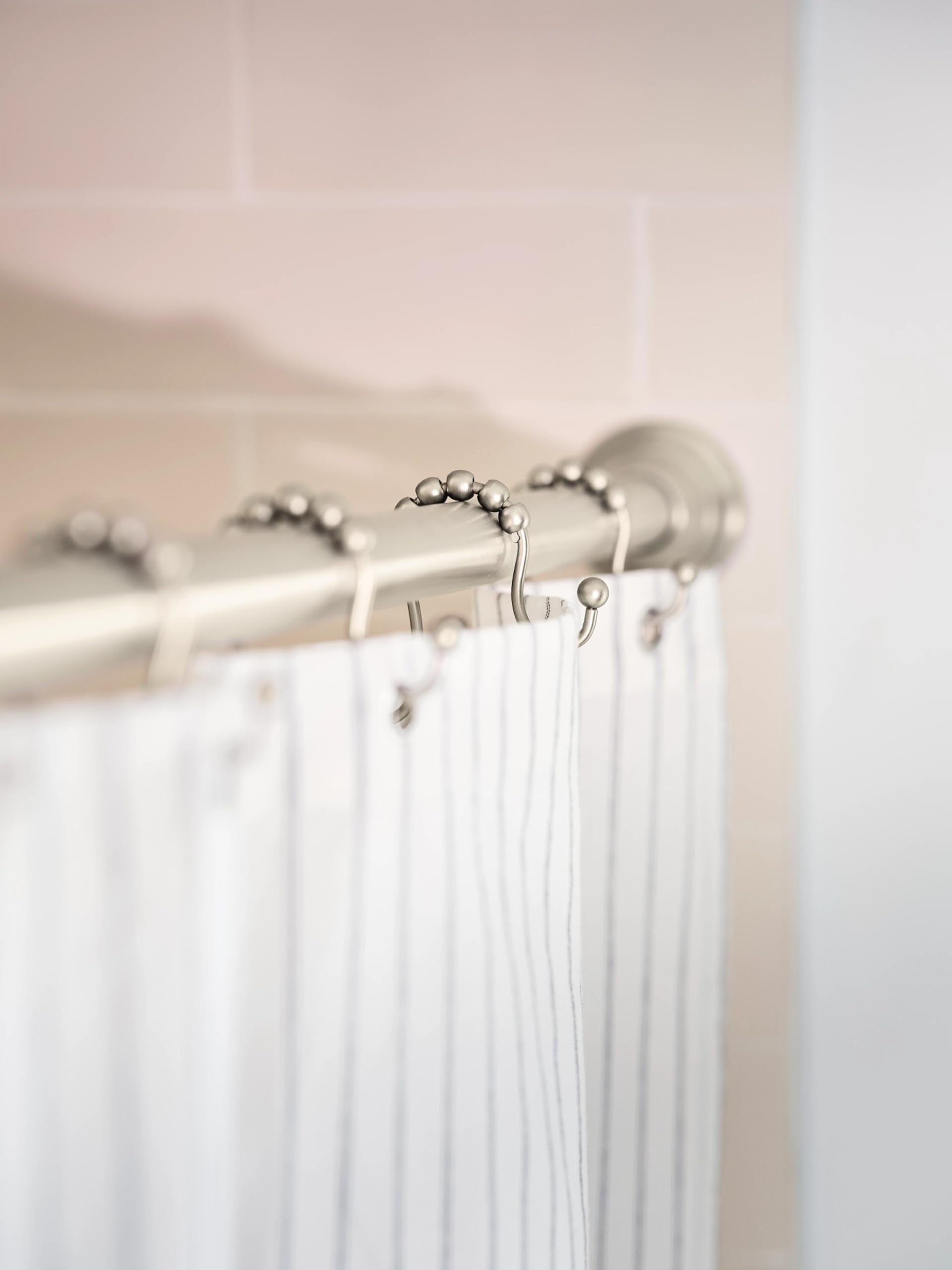 Curved brushed nickel shower rod with ball-shaped rings and white curtain hanging from hooks against bathroom wall.