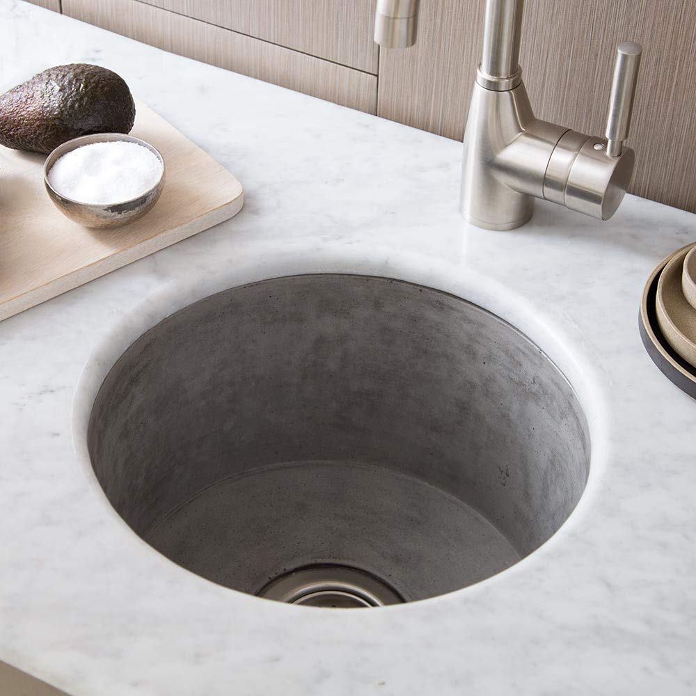 Gray concrete circular prep sink mounted in white marble countertop with stainless steel faucet and wood cabinetry.
