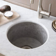 Gray concrete circular prep sink mounted in white marble countertop with stainless steel faucet and wood cabinetry.