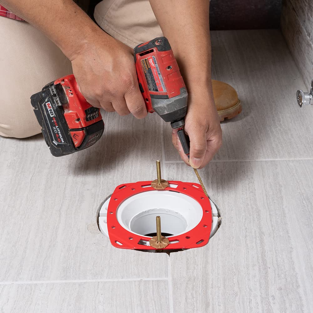 Red toilet flange repair ring being installed around white pipe opening with brass bolts and screws.