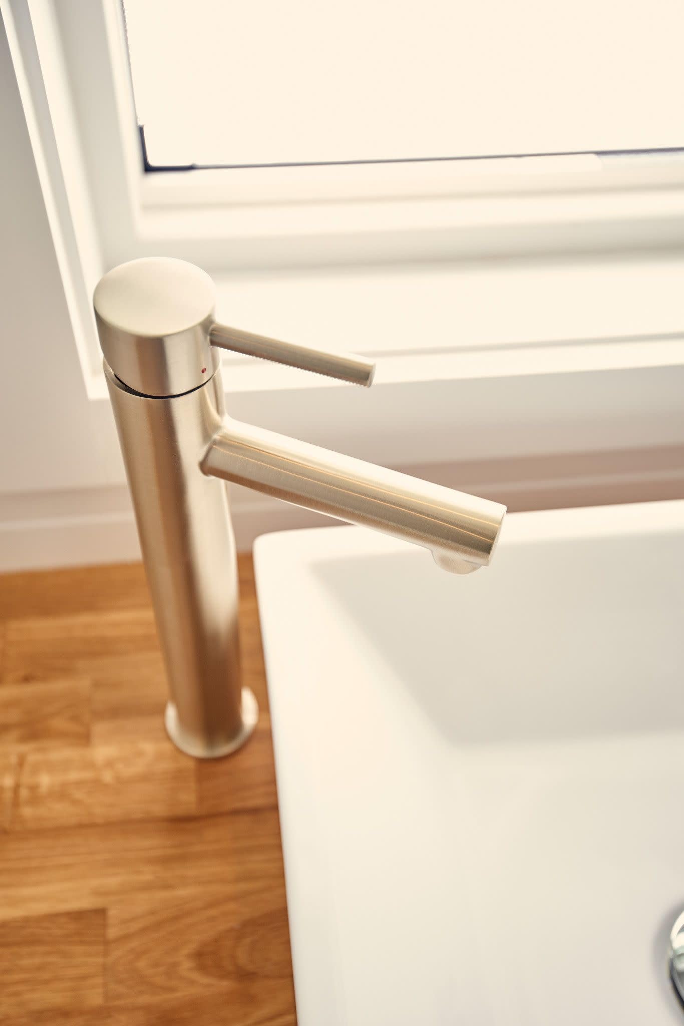 Brushed nickel single-handle bathroom faucet with cylindrical body and curved spout installed on white vessel sink.