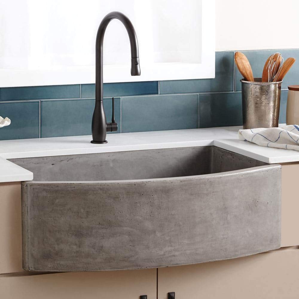 Ash-colored concrete farmhouse sink with curved front, black pull-down faucet, and white countertop.