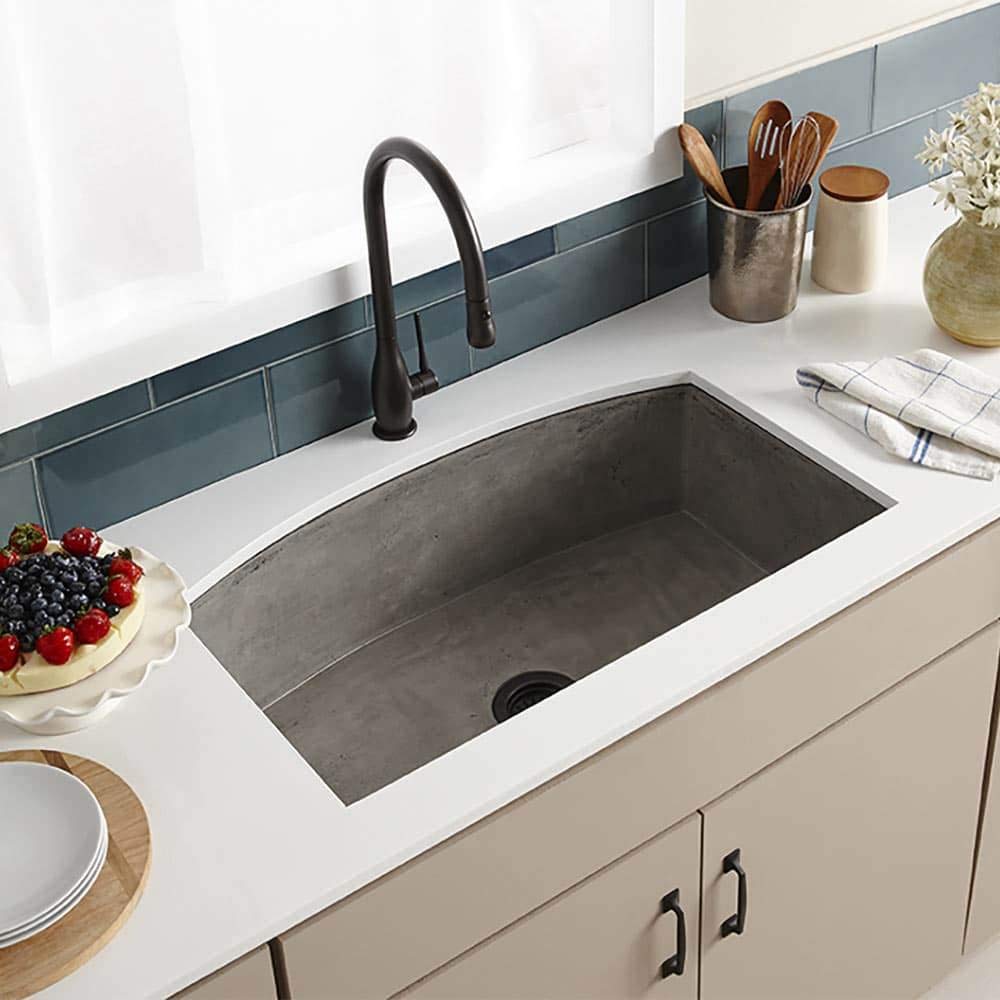 Gray concrete farmhouse kitchen sink with black pull-down faucet installed in white countertop.