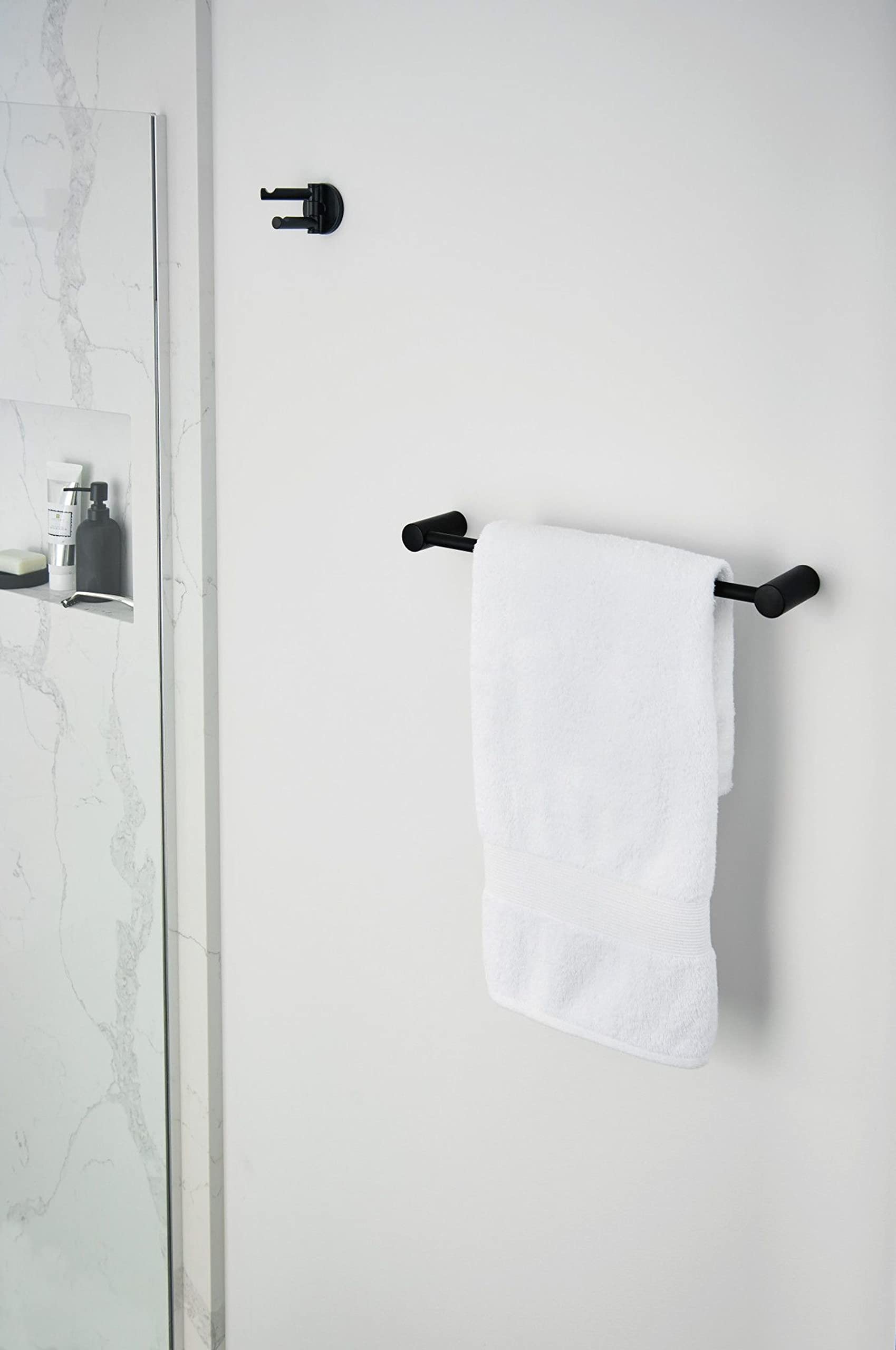 Matte black double swivel robe hooks mounted on marble bathroom wall, one holding white towel.